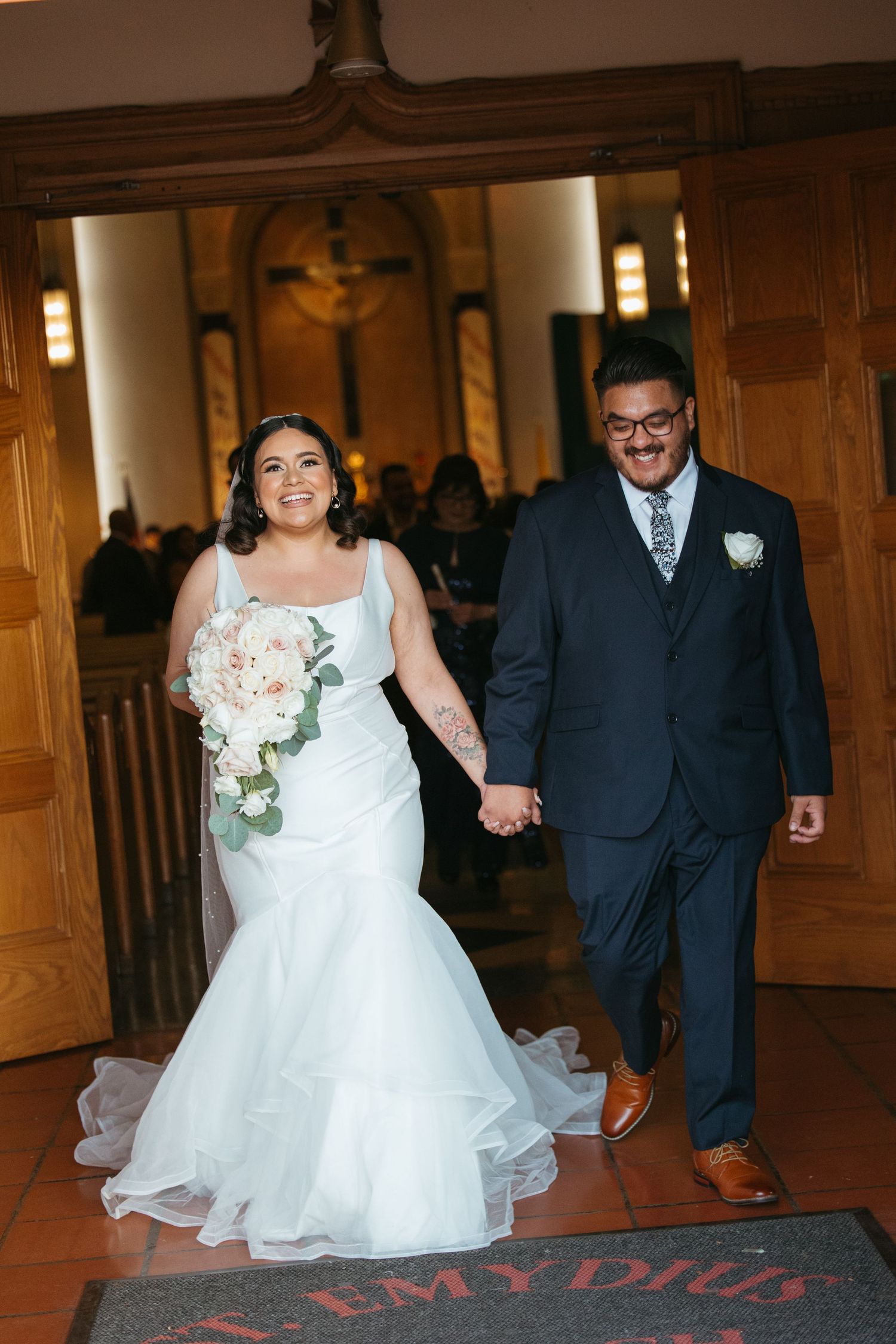 Newlyweds holding hands and smiling as they walk down the church aisle after their wedding ceremony.