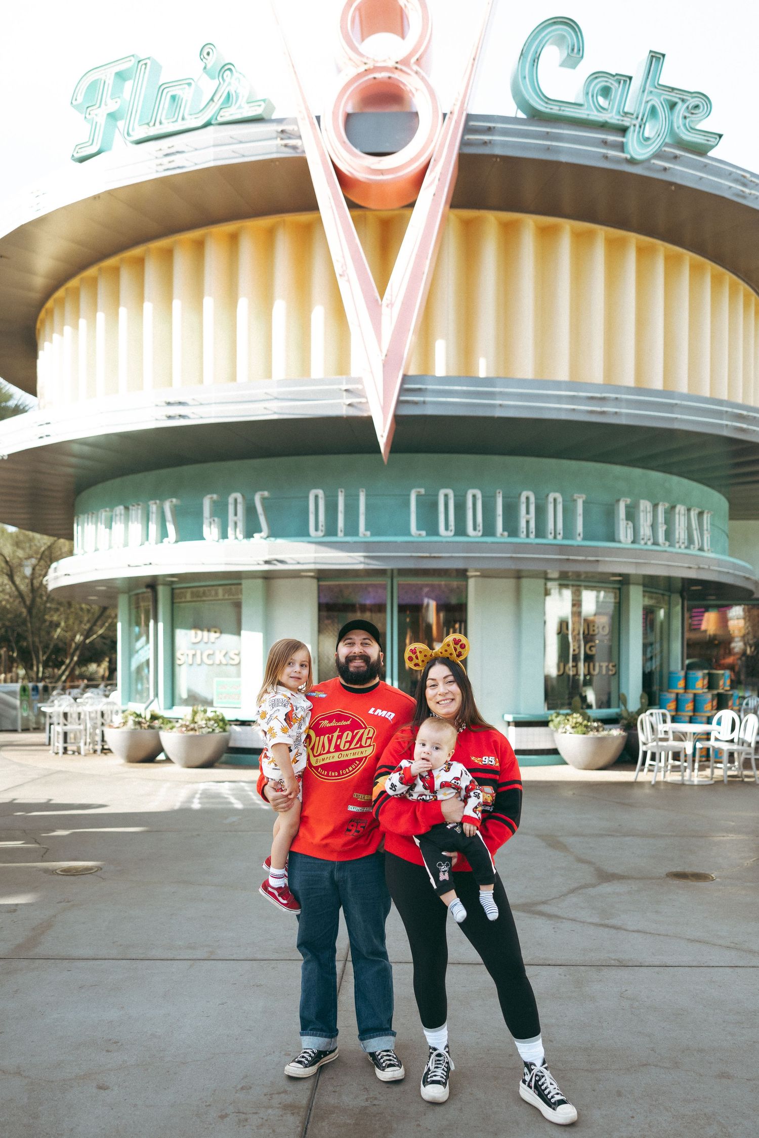 Family posing in matching red outfits in front of Flo's V8 Cafe at Disney California Adventure park.