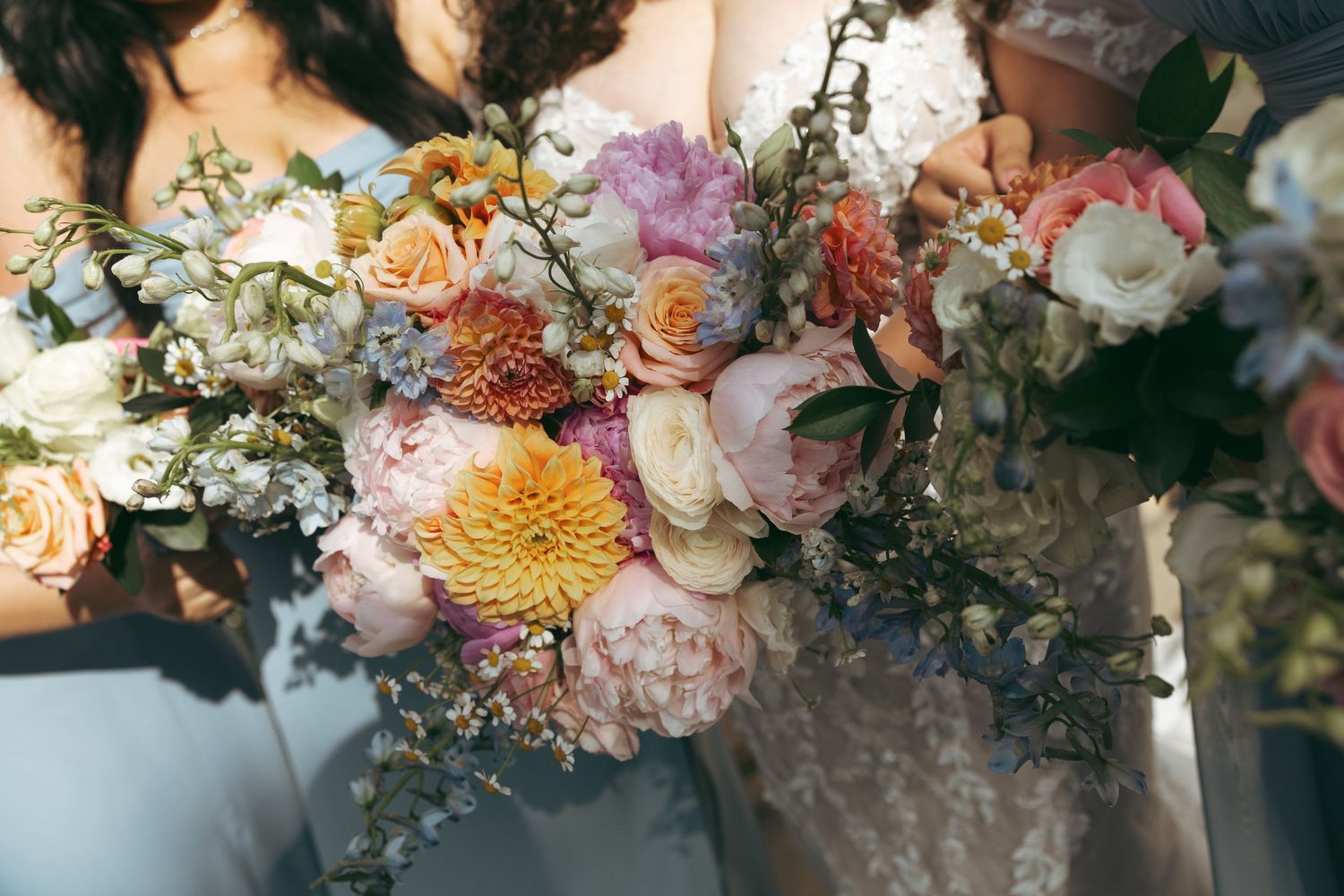 Lush bridal bouquets featuring peonies, dahlias, and roses in peach, pink, and white tones held by bridesmaids.