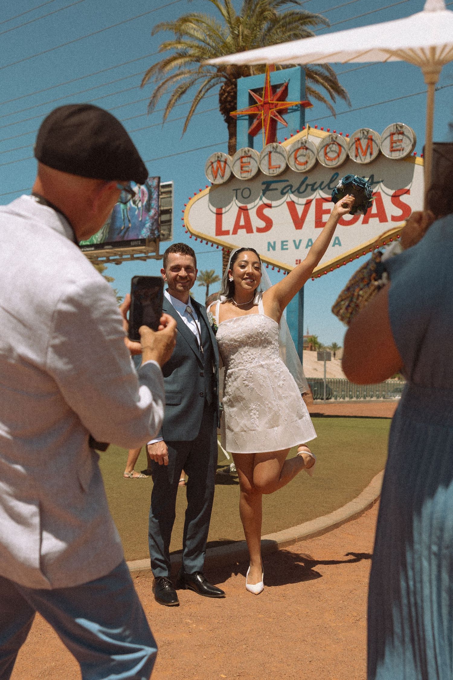 Couple posing in wedding attire in front of the Welcome to Fabulous Las Vegas sign while photographer takes photo.