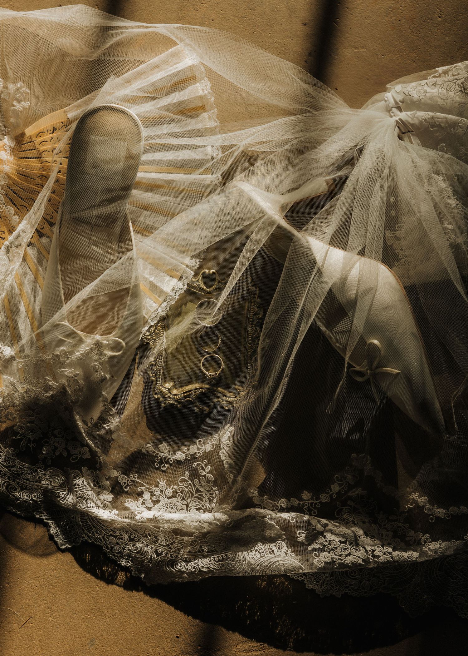 Ethereal wedding veil draped over lace bridal gown with gold rings, bathed in warm golden light.