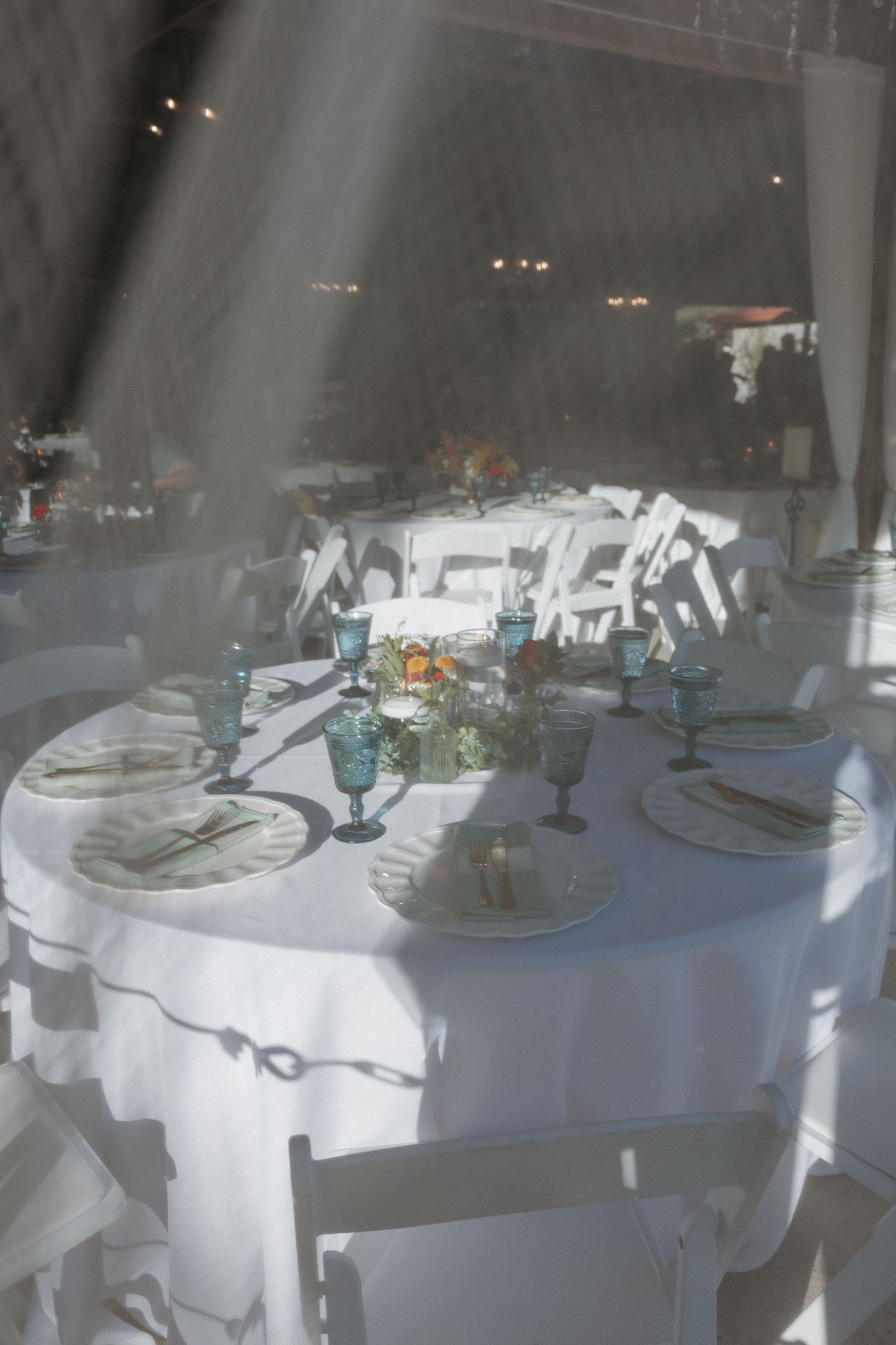 Wedding reception tables with white linens and blue glassware in soft lighting.