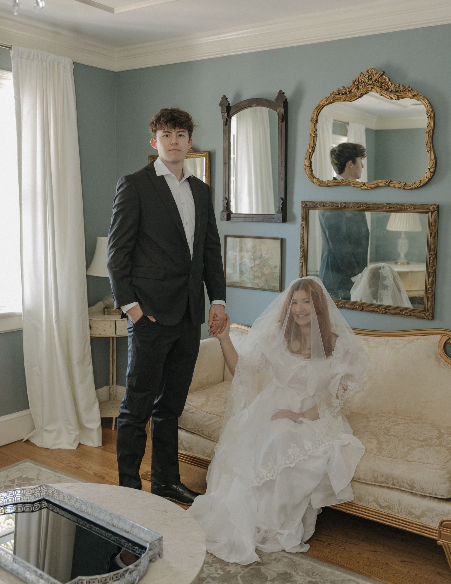 A wedding couple poses in an elegant room with blue walls and ornate gold mirrors during their photo session.