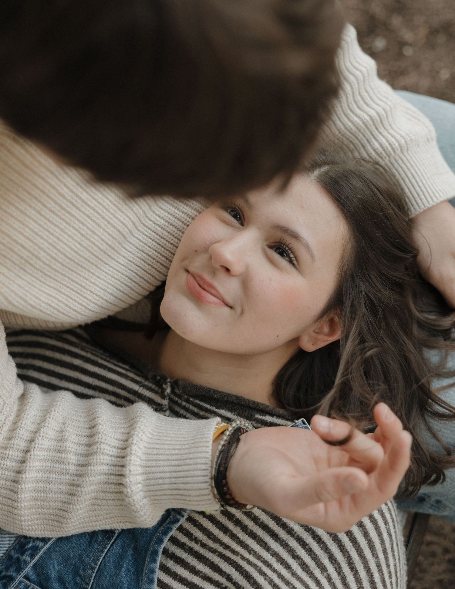 Person wearing a cream sweater lying down and smiling while relaxing on a couch.
