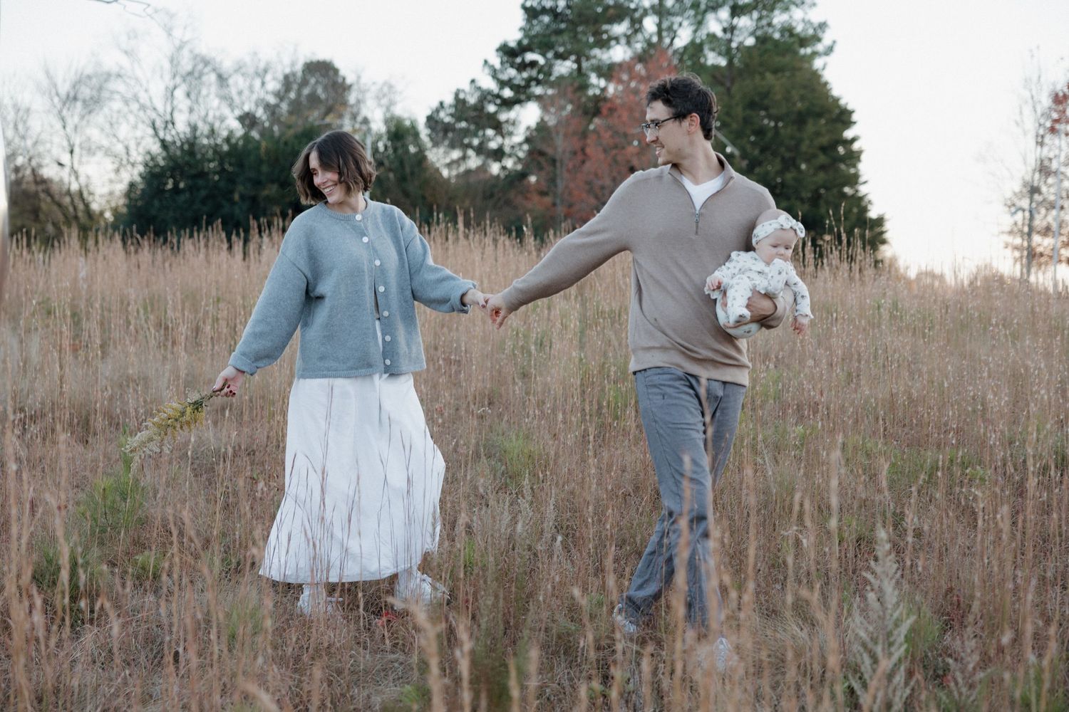 Two people dance together in a golden field of tall grass during sunset.