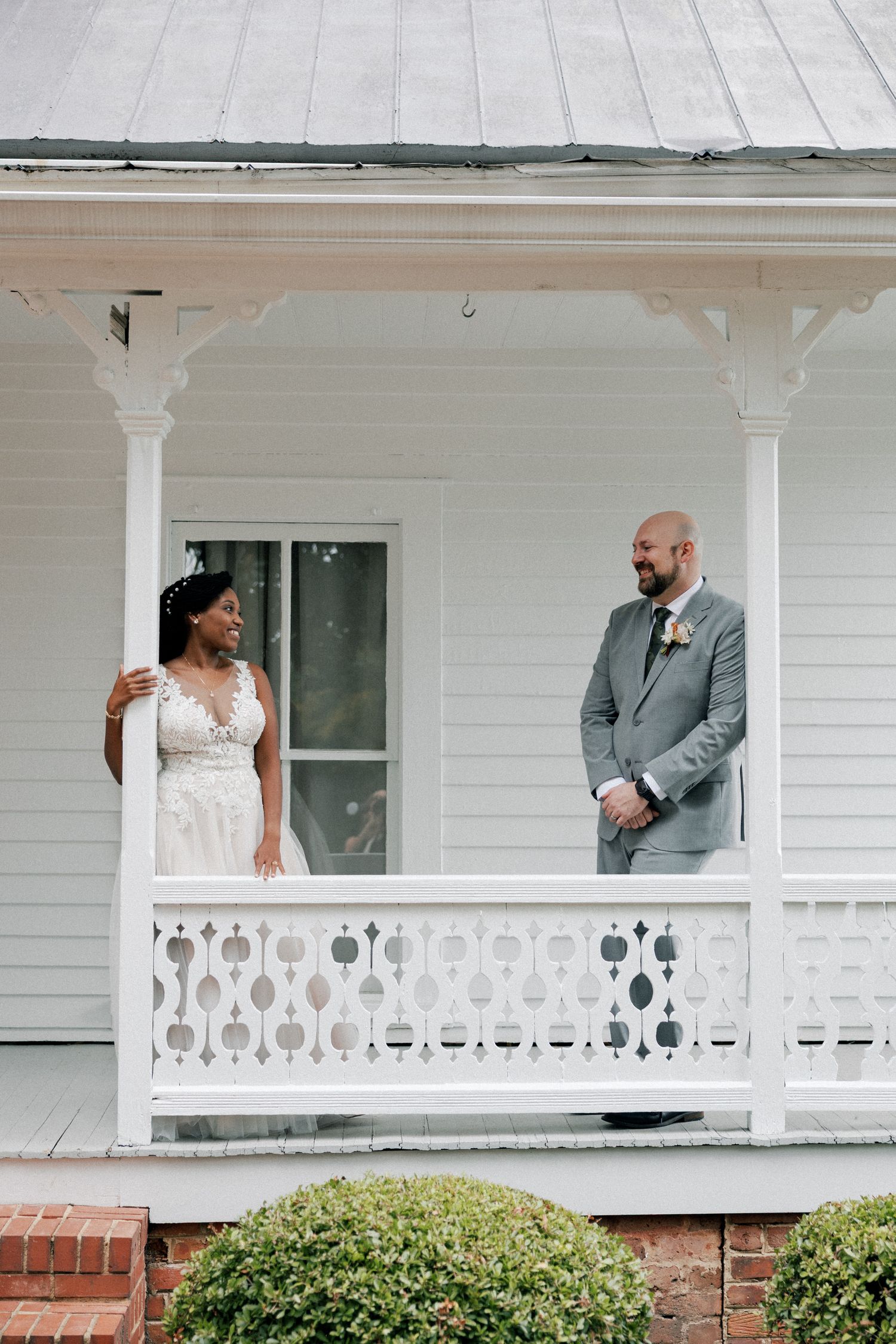 Wedding couple posing on classic white porch with decorative railings.