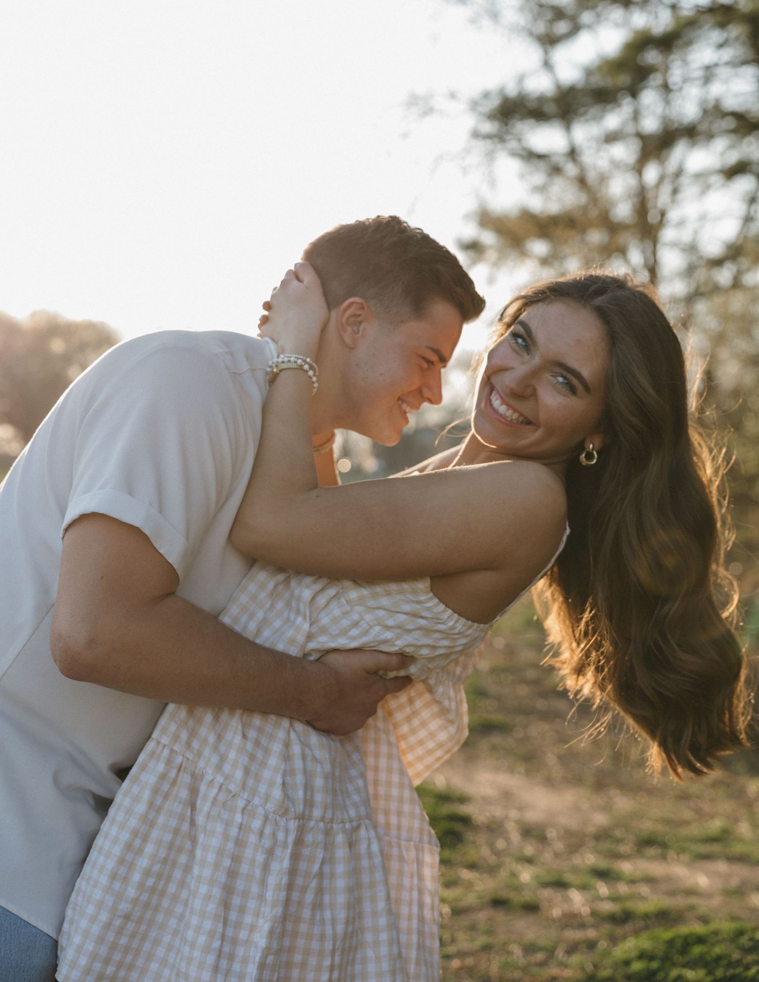 A romantic couple embraces in a sun-drenched field during golden hour creating a dreamy outdoor photoshoot moment.