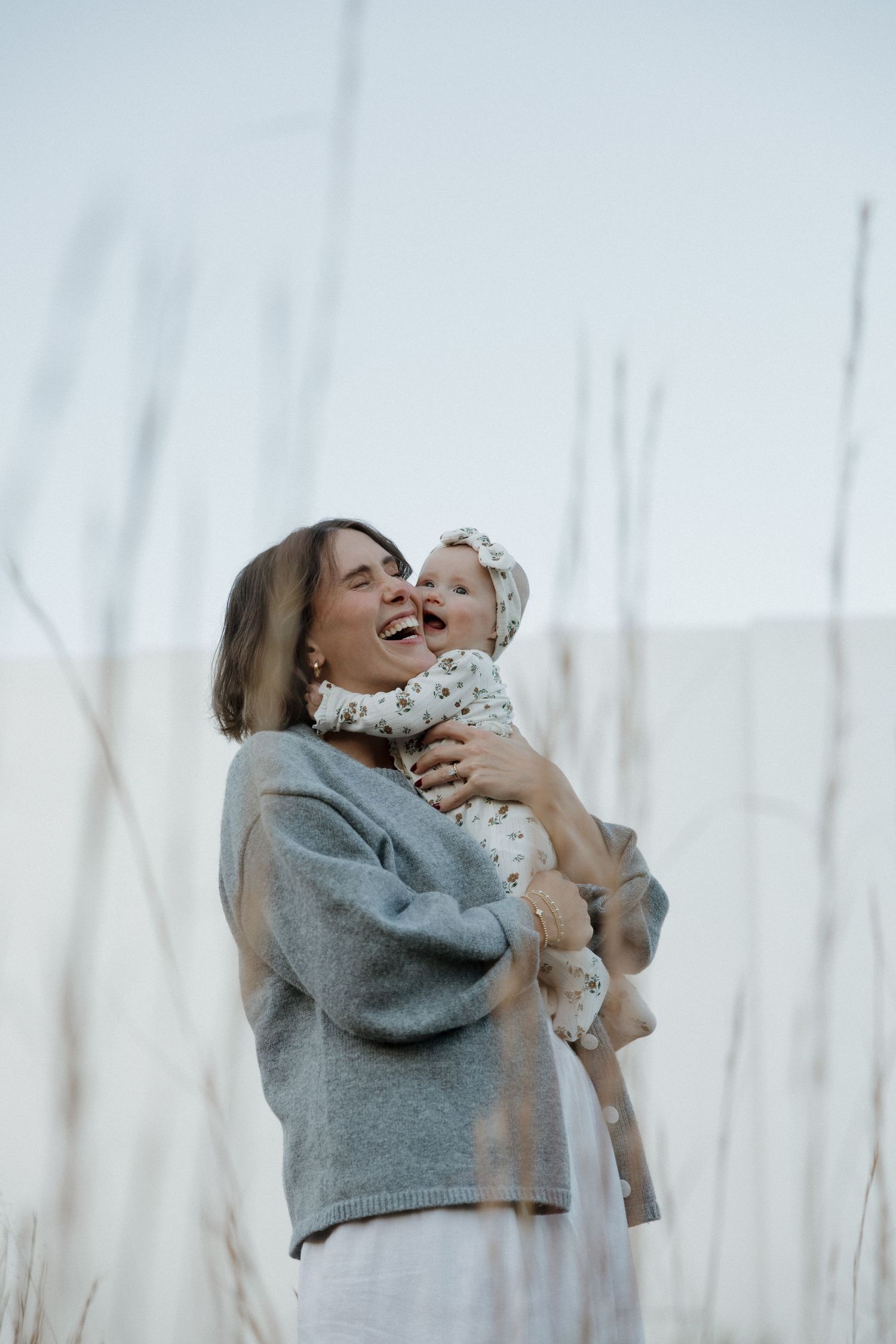 A person in a gray sweater joyfully holds and plays with a small child against a light, airy background.