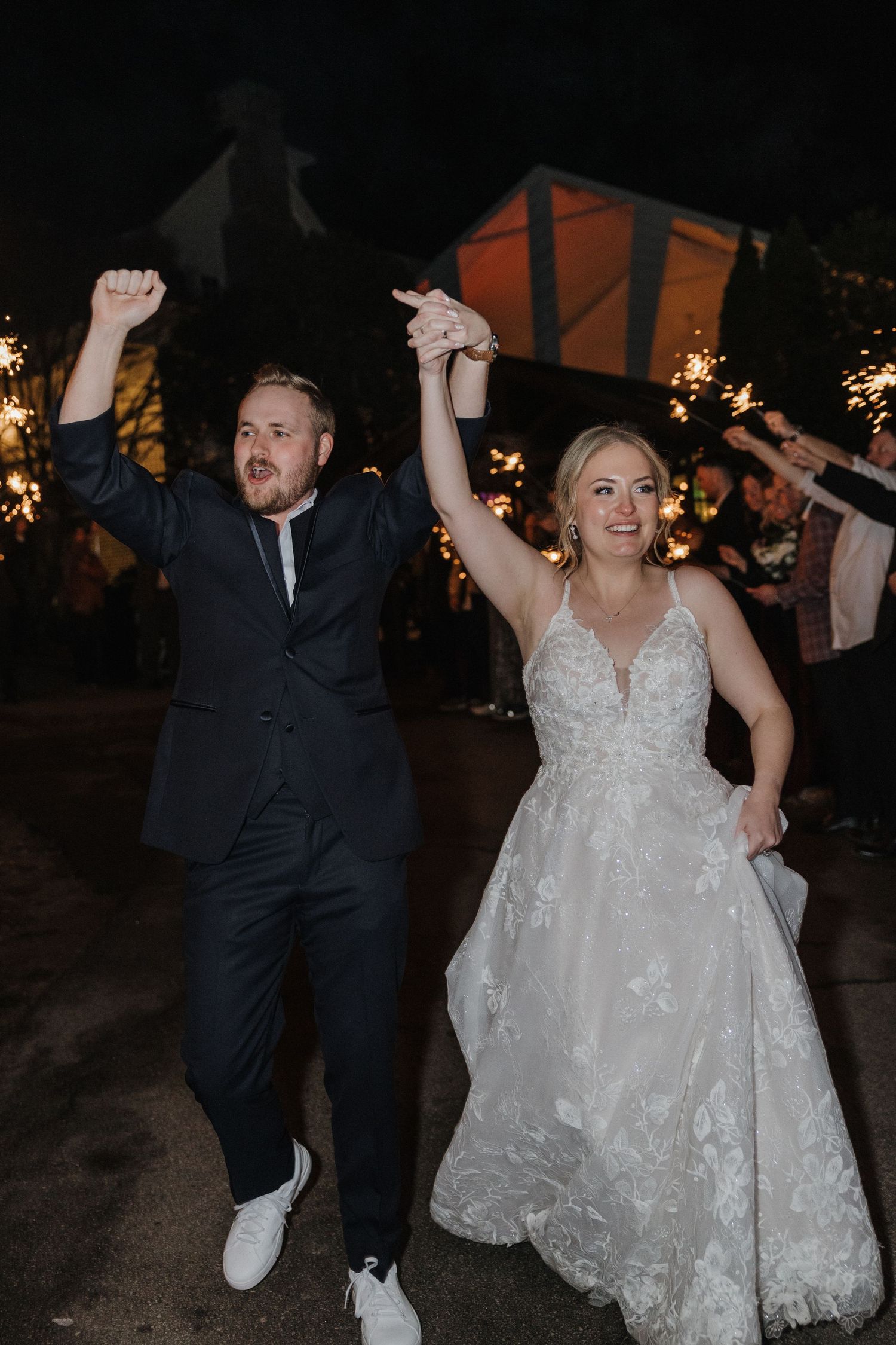 Bride and groom celebrate joyfully with raised hands during sparkler exit at their wedding reception.