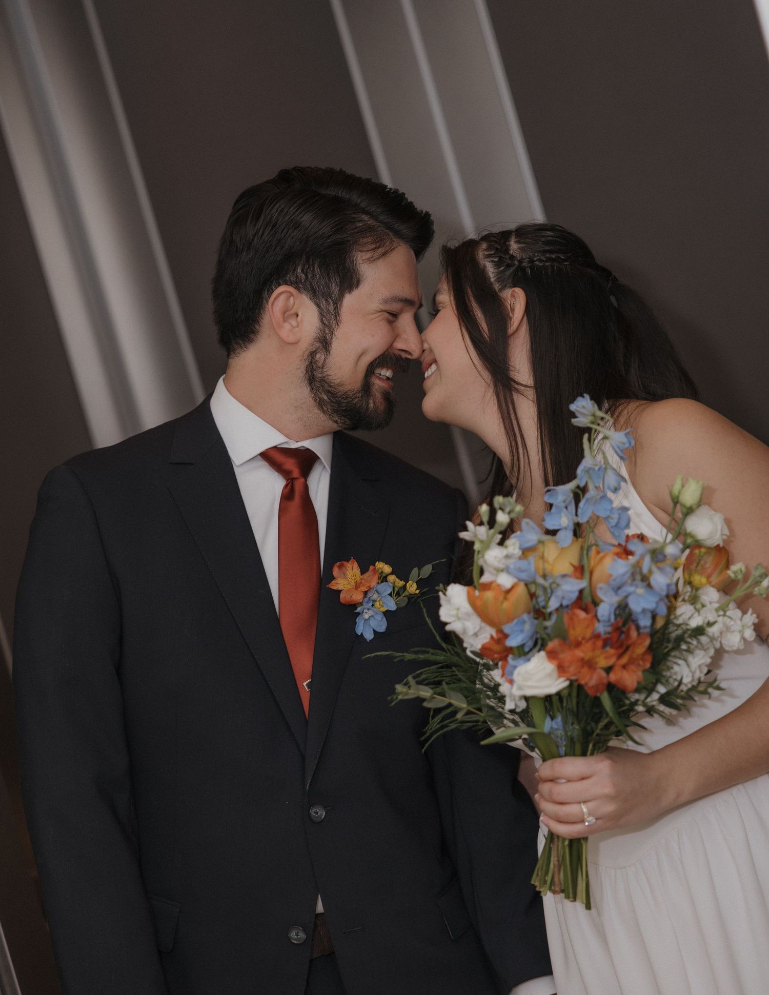 A wedding couple shares an intimate moment while holding a vibrant bouquet of orange and blue flowers.