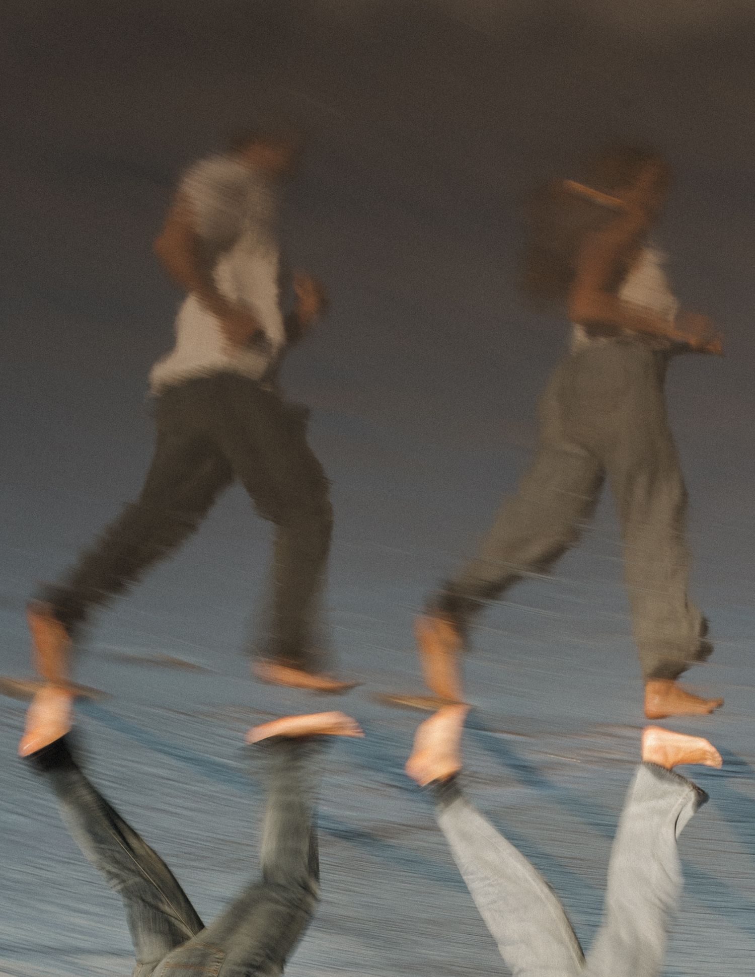 Two blurred figures running barefoot on a reflective surface, captured with motion blur effect.
