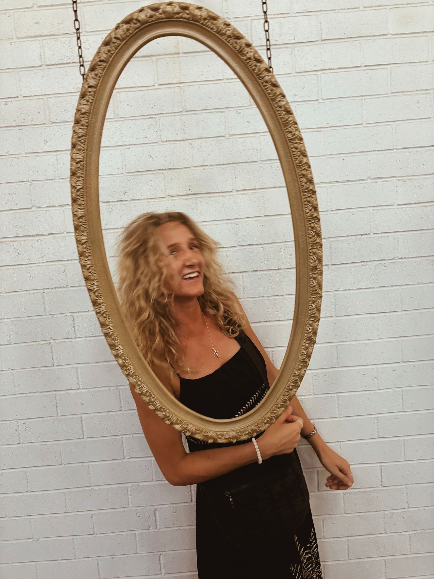 Decorative oval gold mirror mounted on white brick wall creates playful sequential reflections.