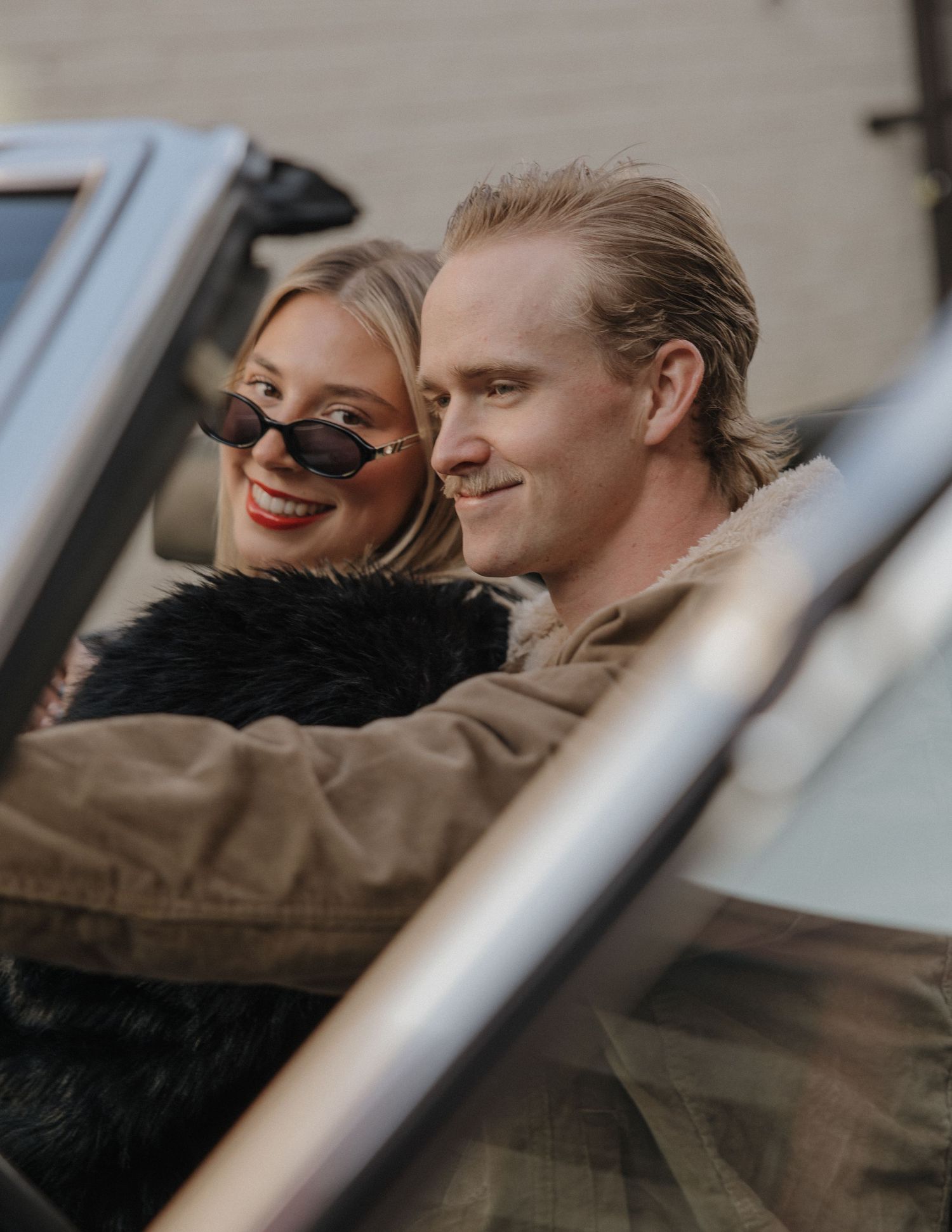A couple relaxes together in a car, sharing a warm moment through the window frame.
