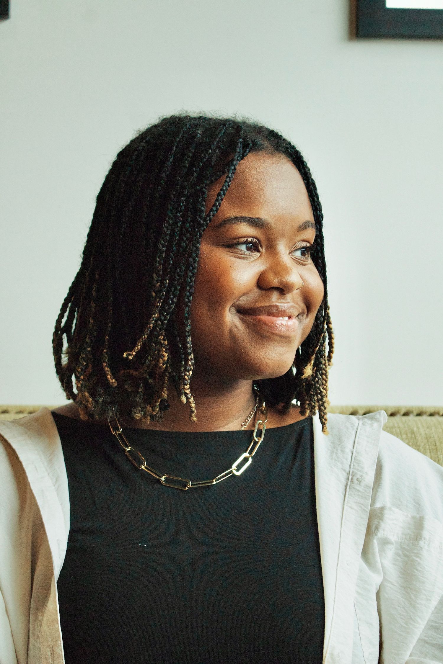 Portrait showing bright smile wearing black top and white blazer with chain necklace.