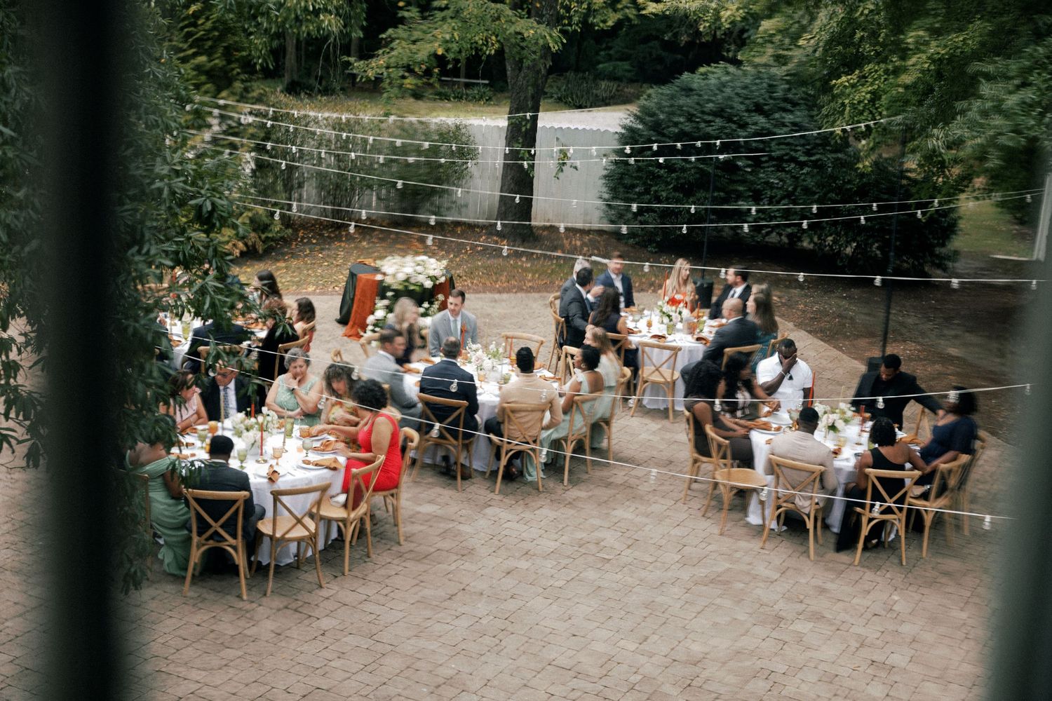 Outdoor wedding reception with string lights and guests seated at long tables.