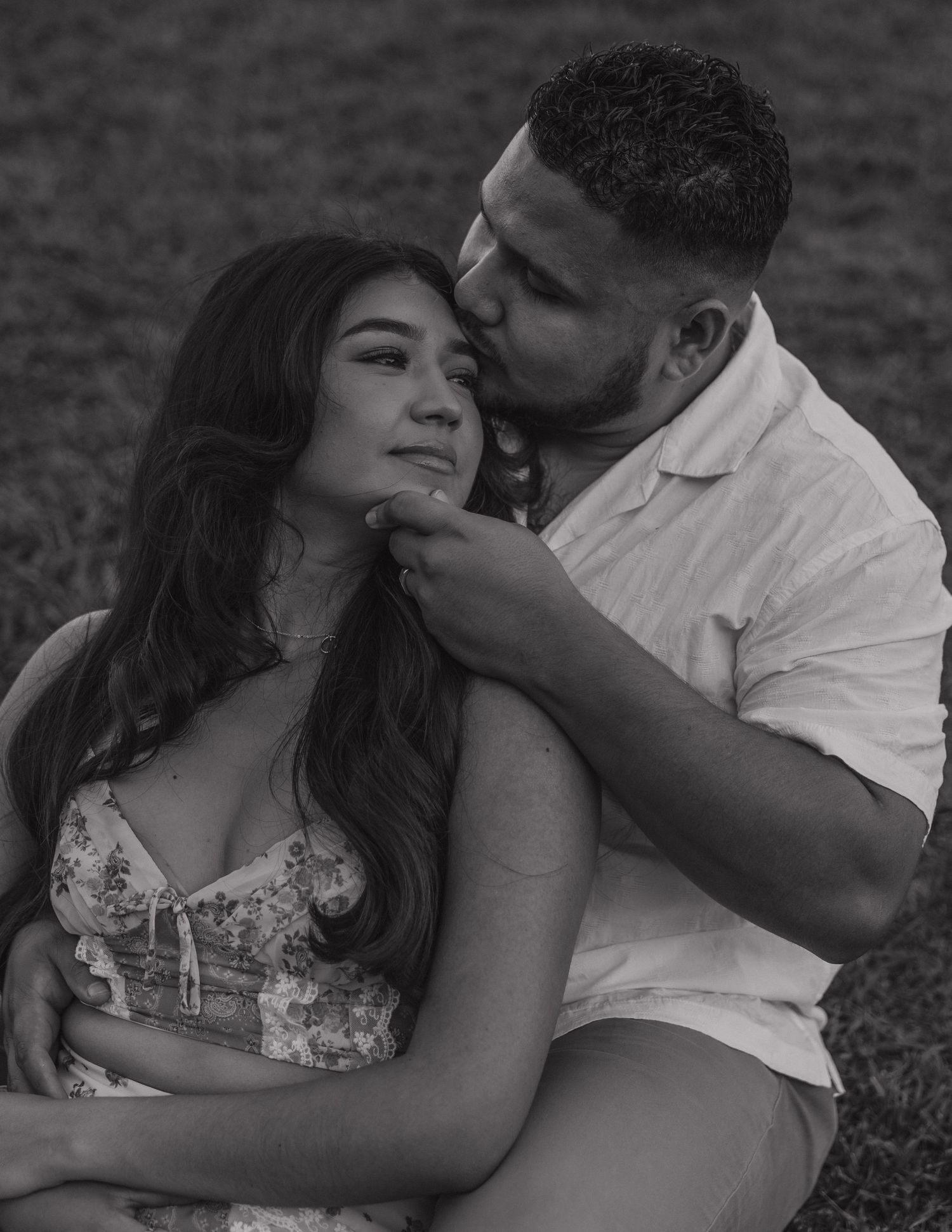 Black and white photo of a romantic couple sitting outdoors, man kissing womans cheek tenderly.