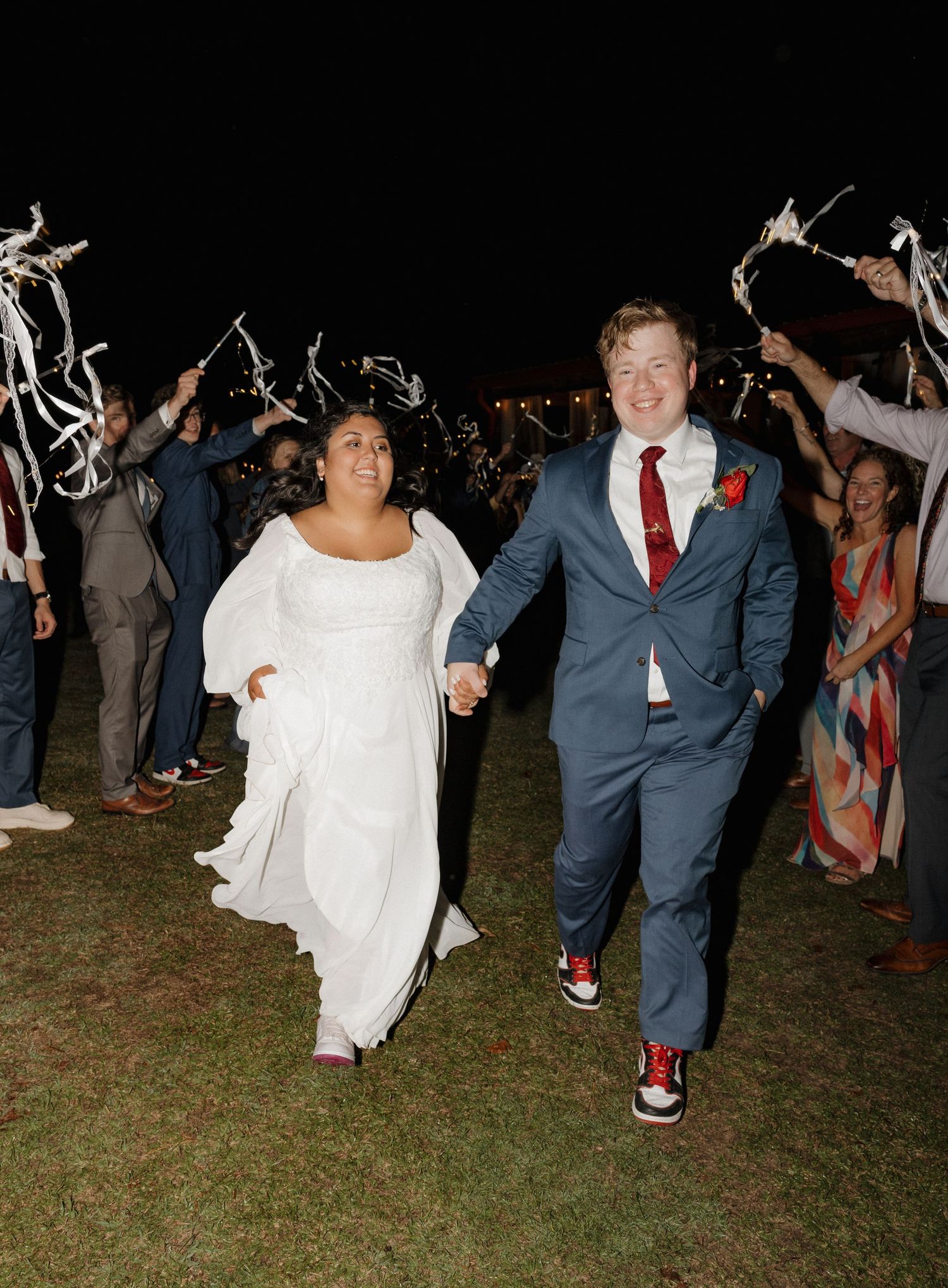 Wedding party dancing outdoors at night on grass with joyful expressions.