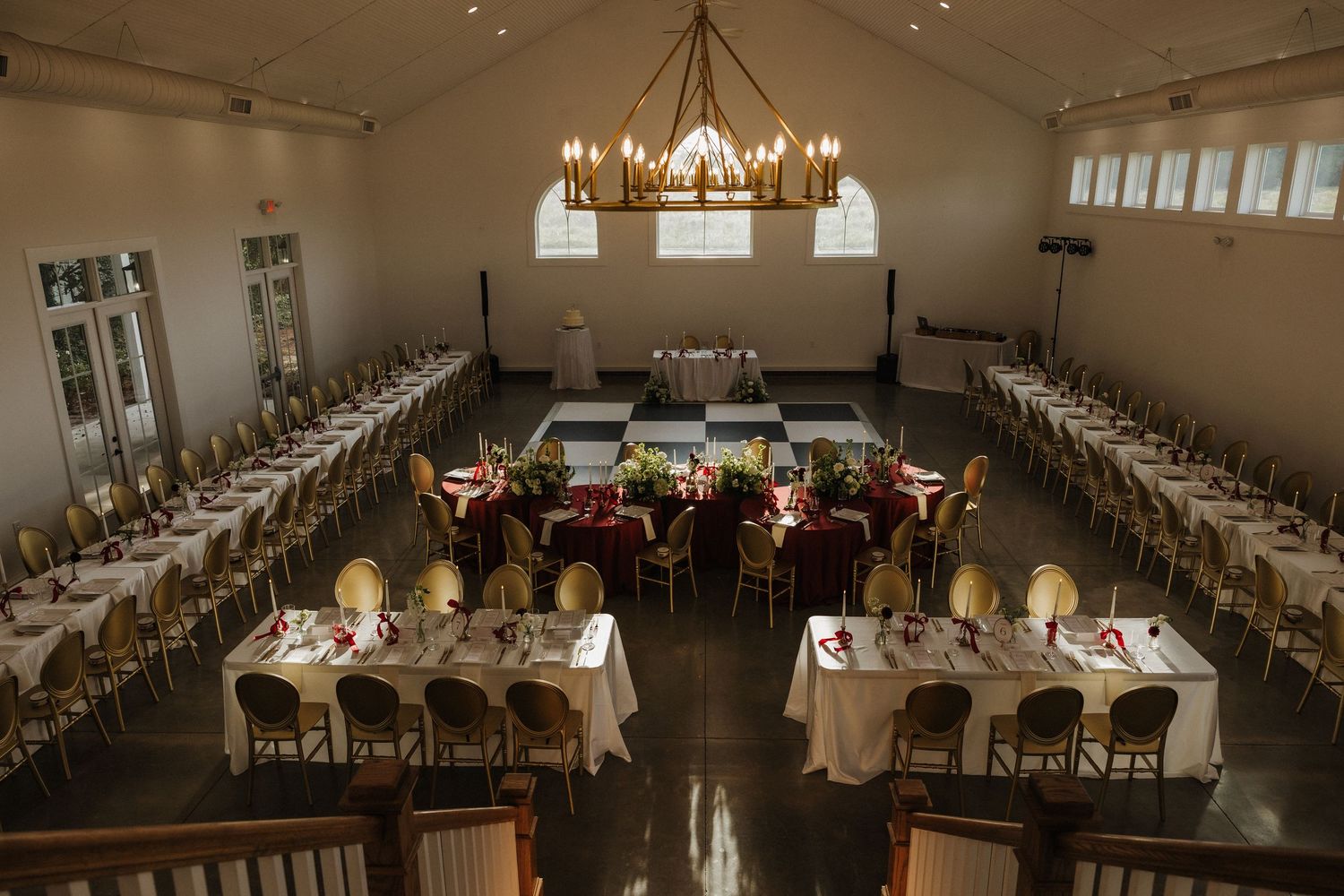 Elegant banquet hall with chandelier, long dining tables set with white linens and floral centerpieces for a wedding reception.