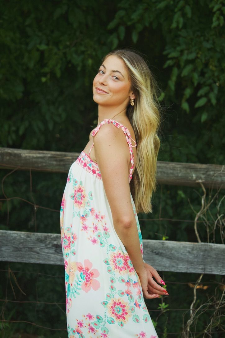 Woman in floral summer dress posing by wooden fence in garden setting.