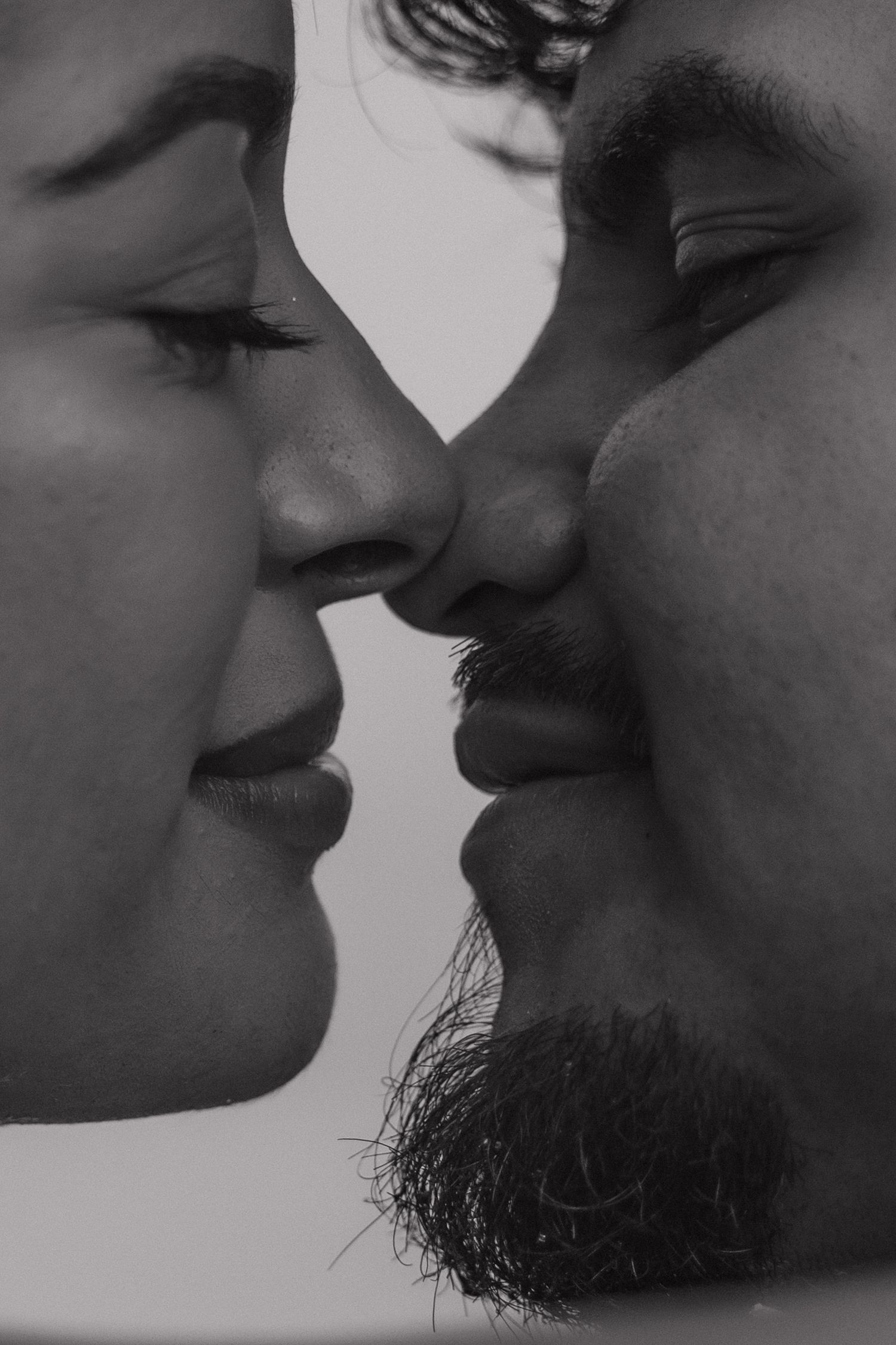 Black and white close-up profile of a man with beard and woman about to kiss, romantic couple portrait.