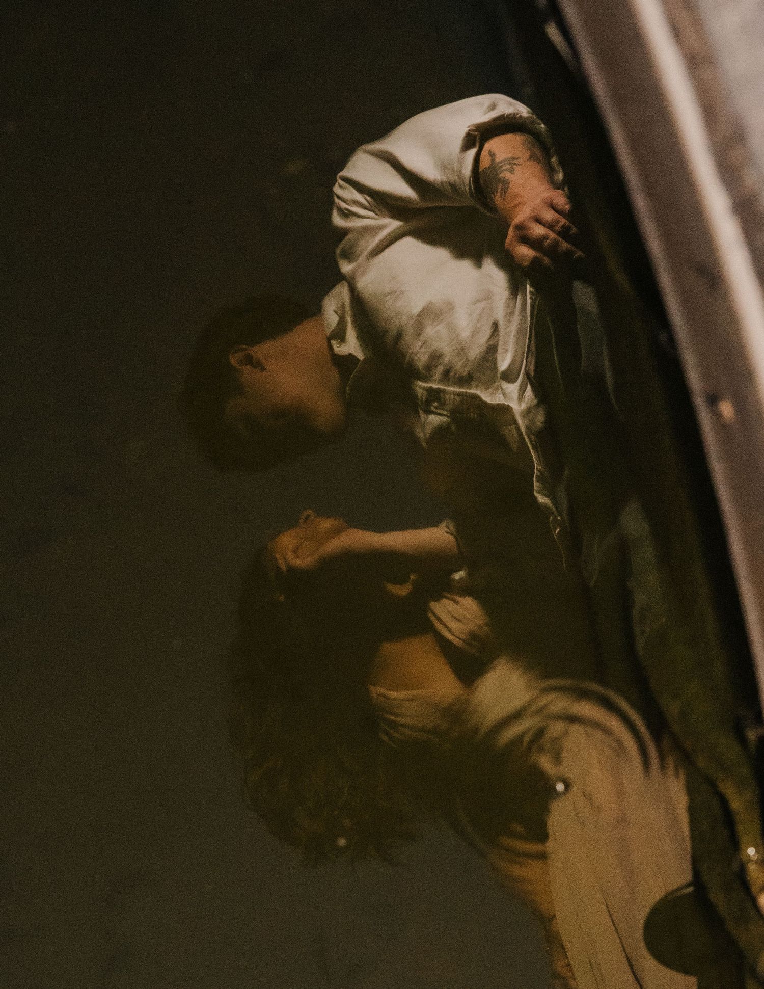 Two figures in dramatic lighting, one inverted, wearing period clothing in a dark, cinematic scene.