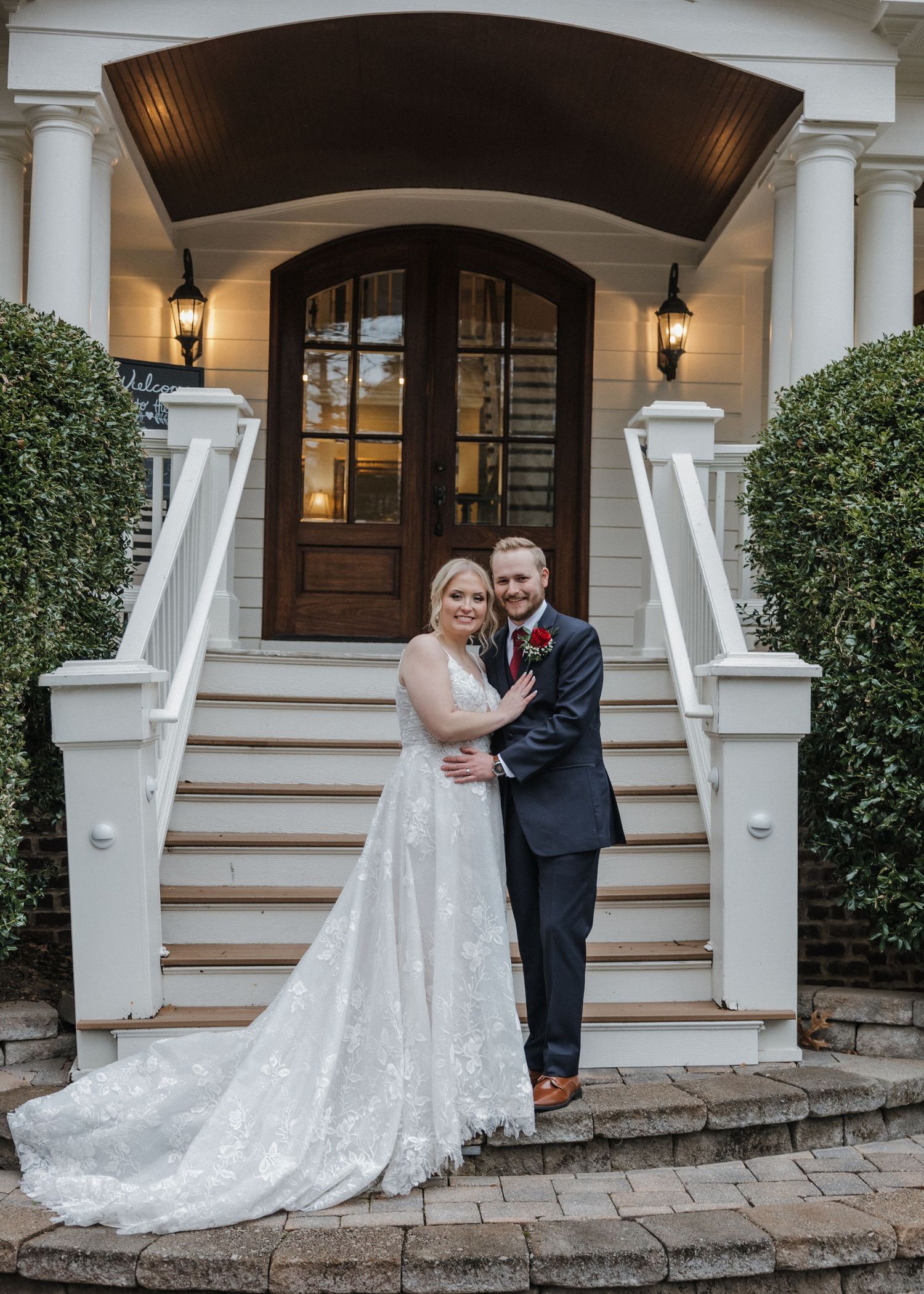 Bride and groom pose on elegant white staircase steps outside a classic venue on their wedding day.