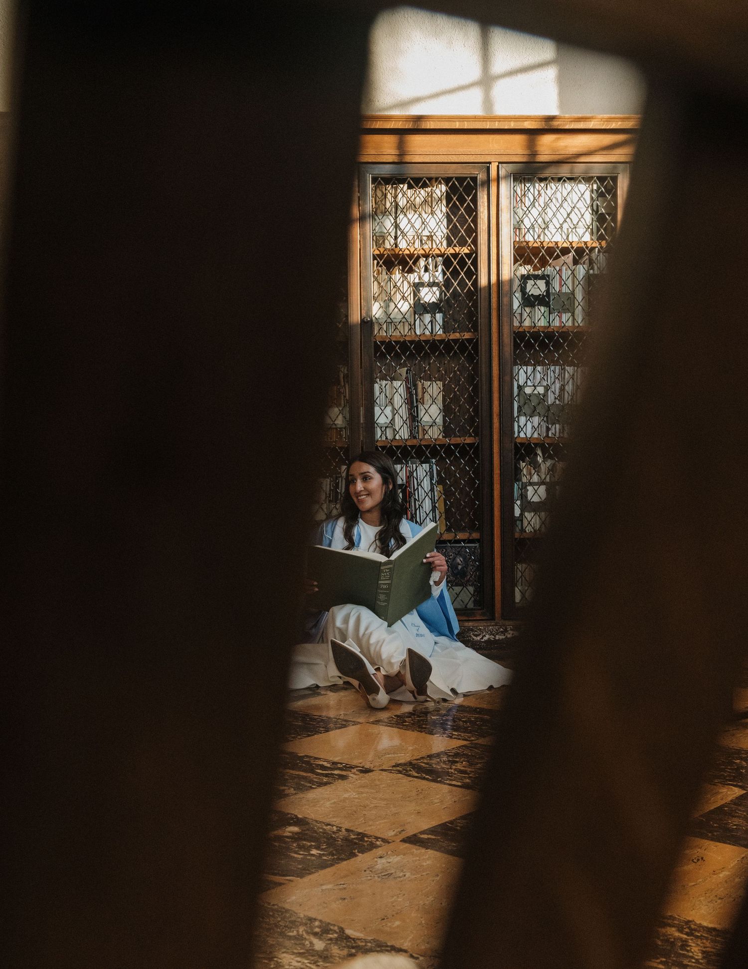 Woman sitting on floor reading a book, framed by wooden elements in a sunlit vintage interior.