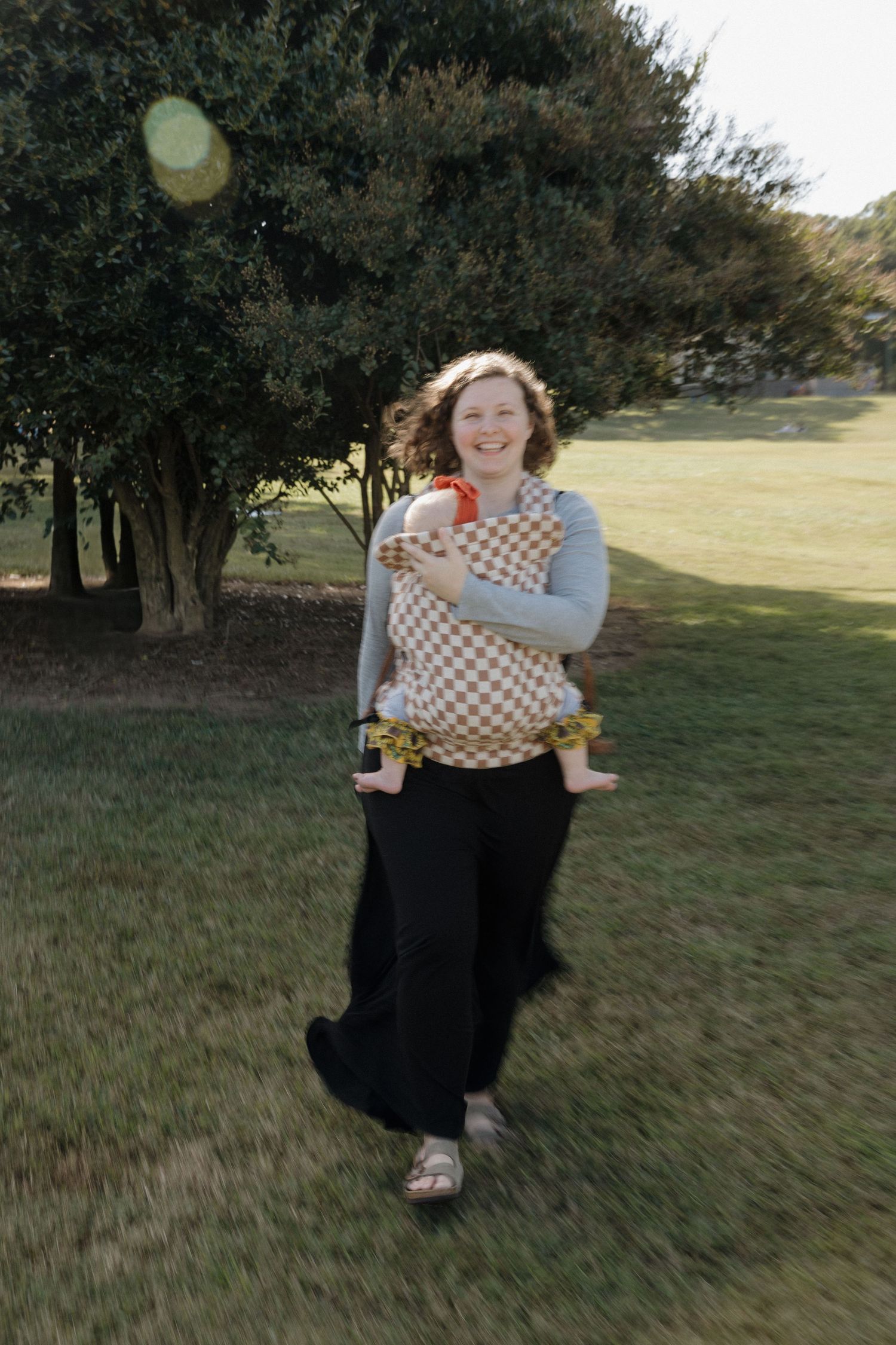 A person in a polka dot top and black skirt twirls joyfully in a grassy field on a sunny day.