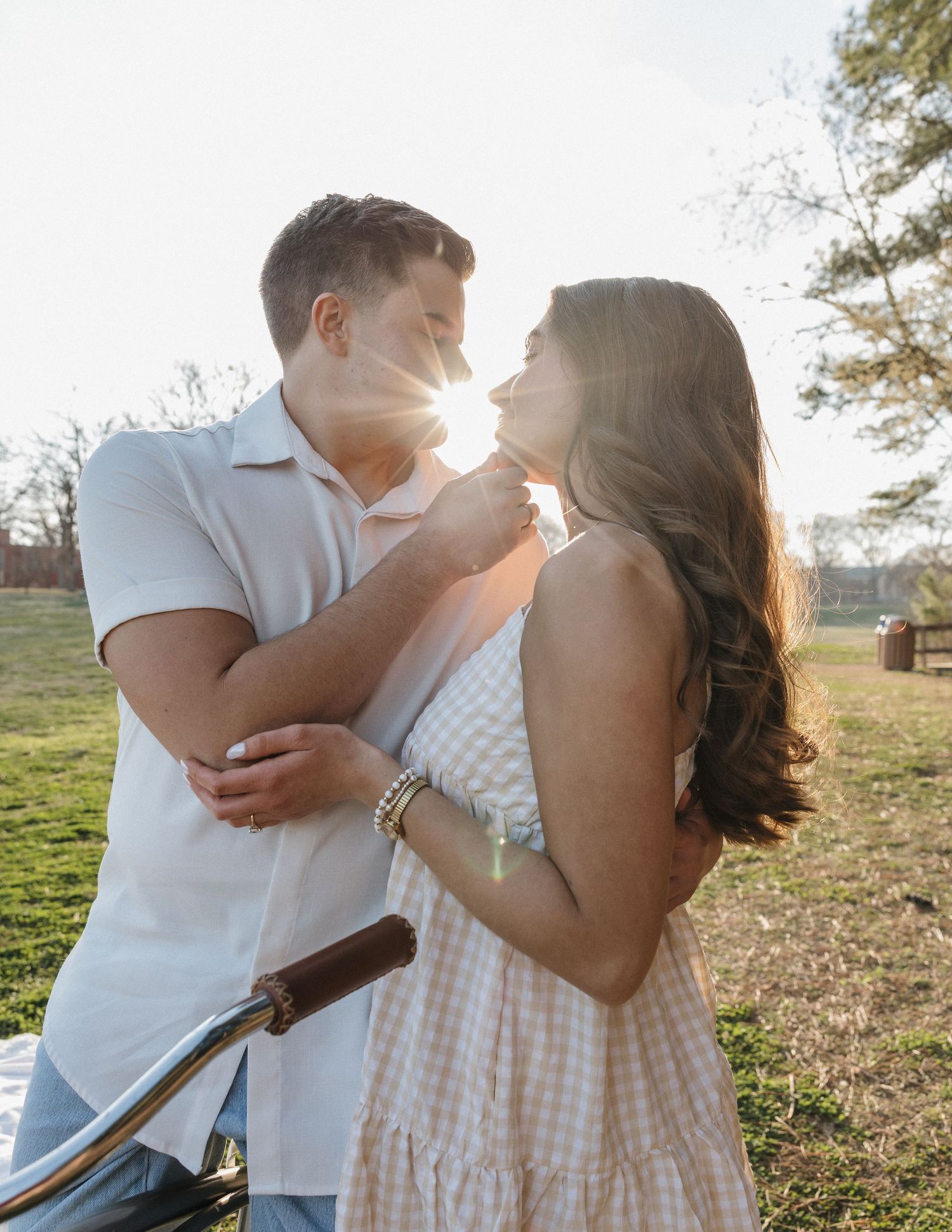 A couple shares a romantic moment outdoors at golden hour, with sunlight glowing between them in a sunny park.