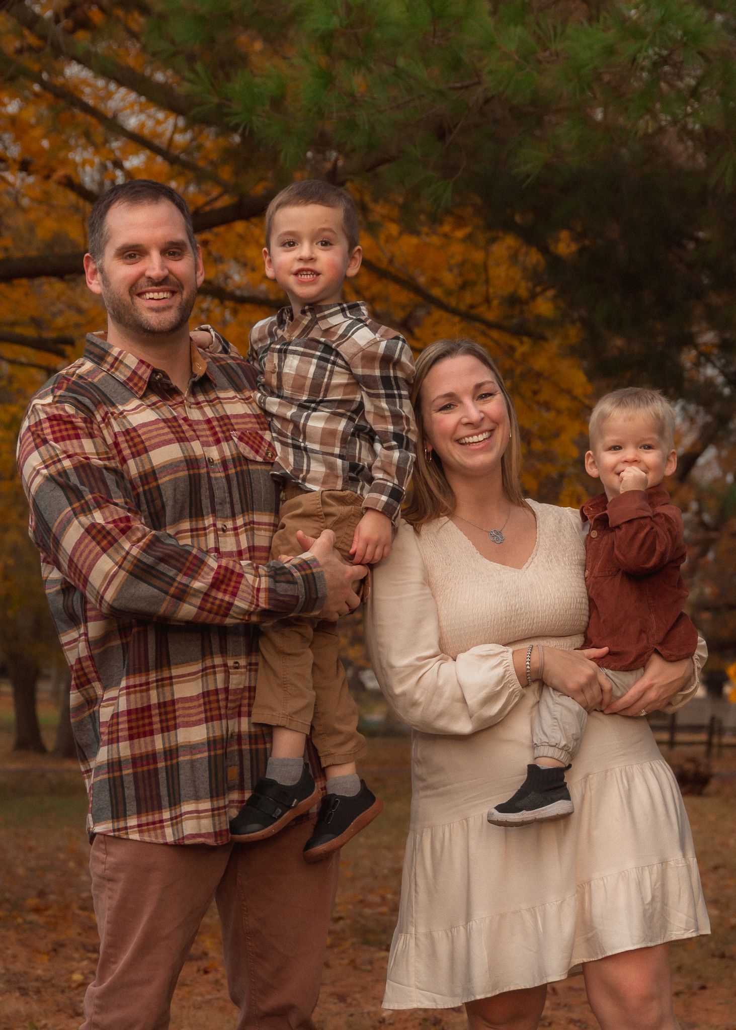 A family in coordinating cream and brown outfits poses together during an autumn photoshoot in a park setting.