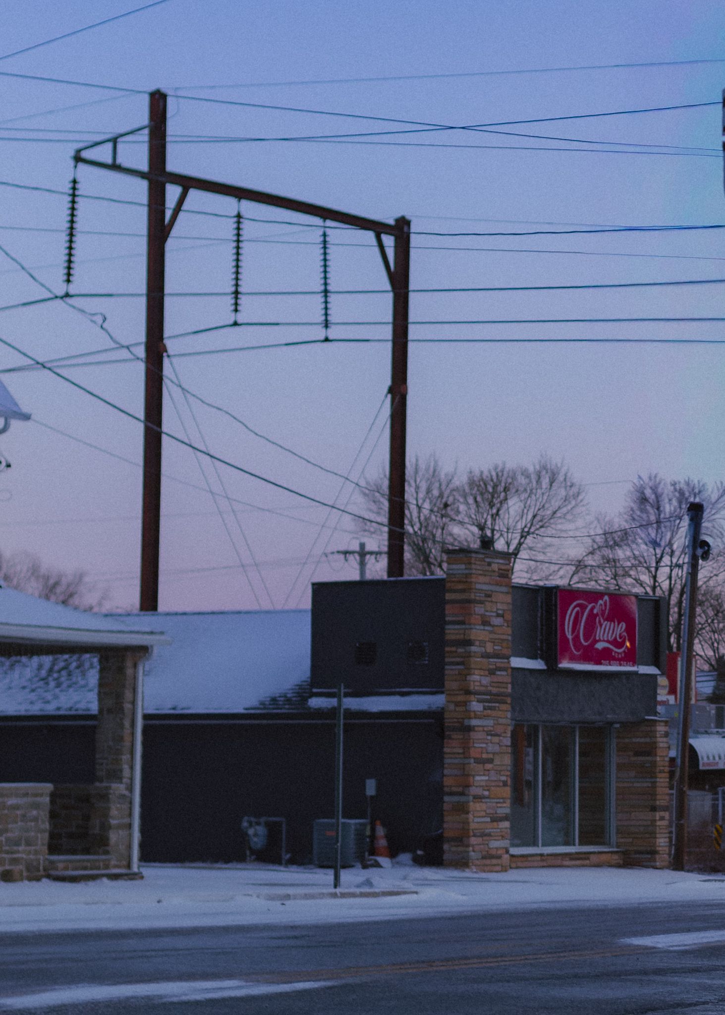 A panoramic view of a strip mall building with power lines overhead and a brick facade against an evening sky.