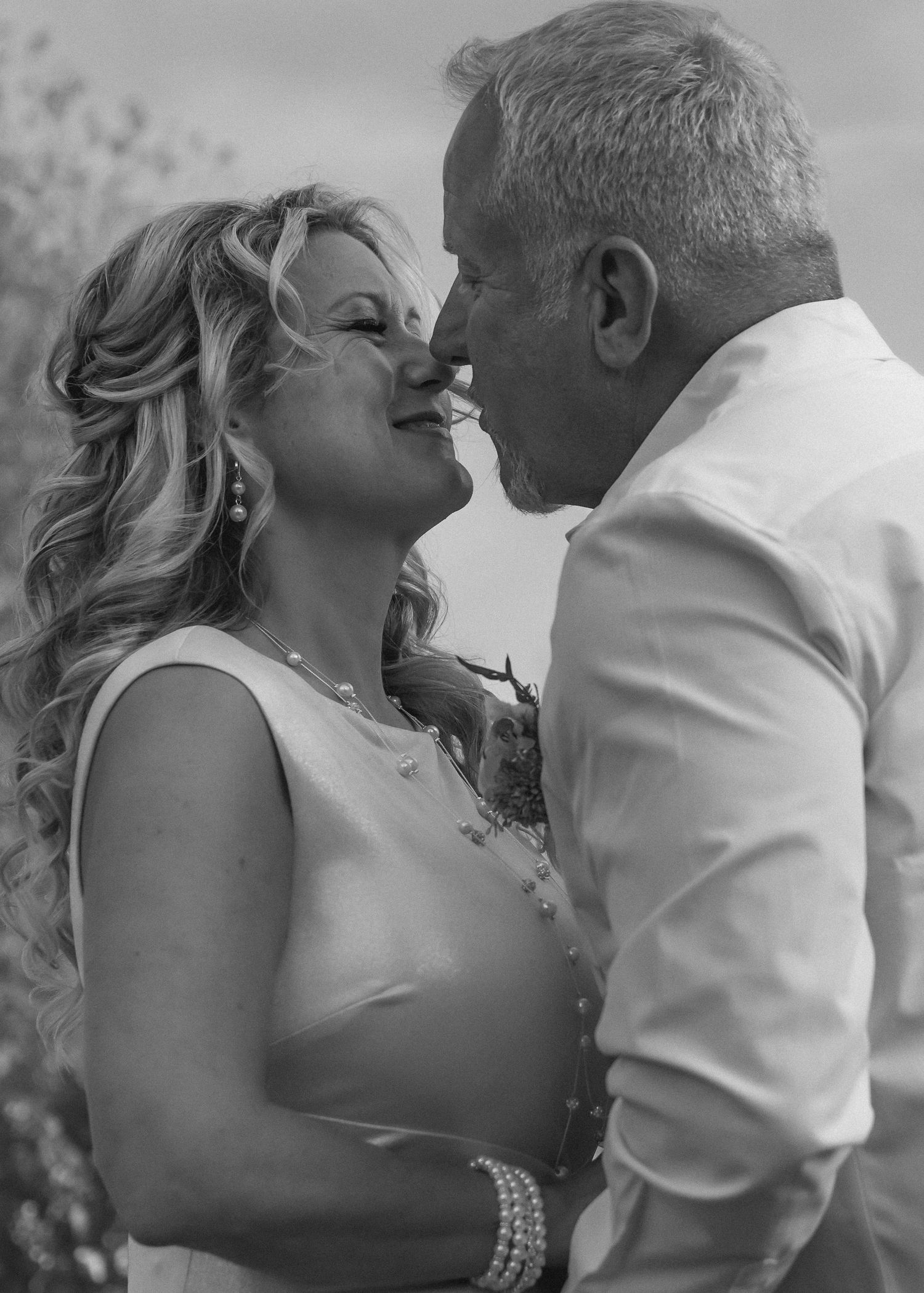 A romantic black and white portrait of a couple in an intimate moment outdoors, with the woman wearing pearls.