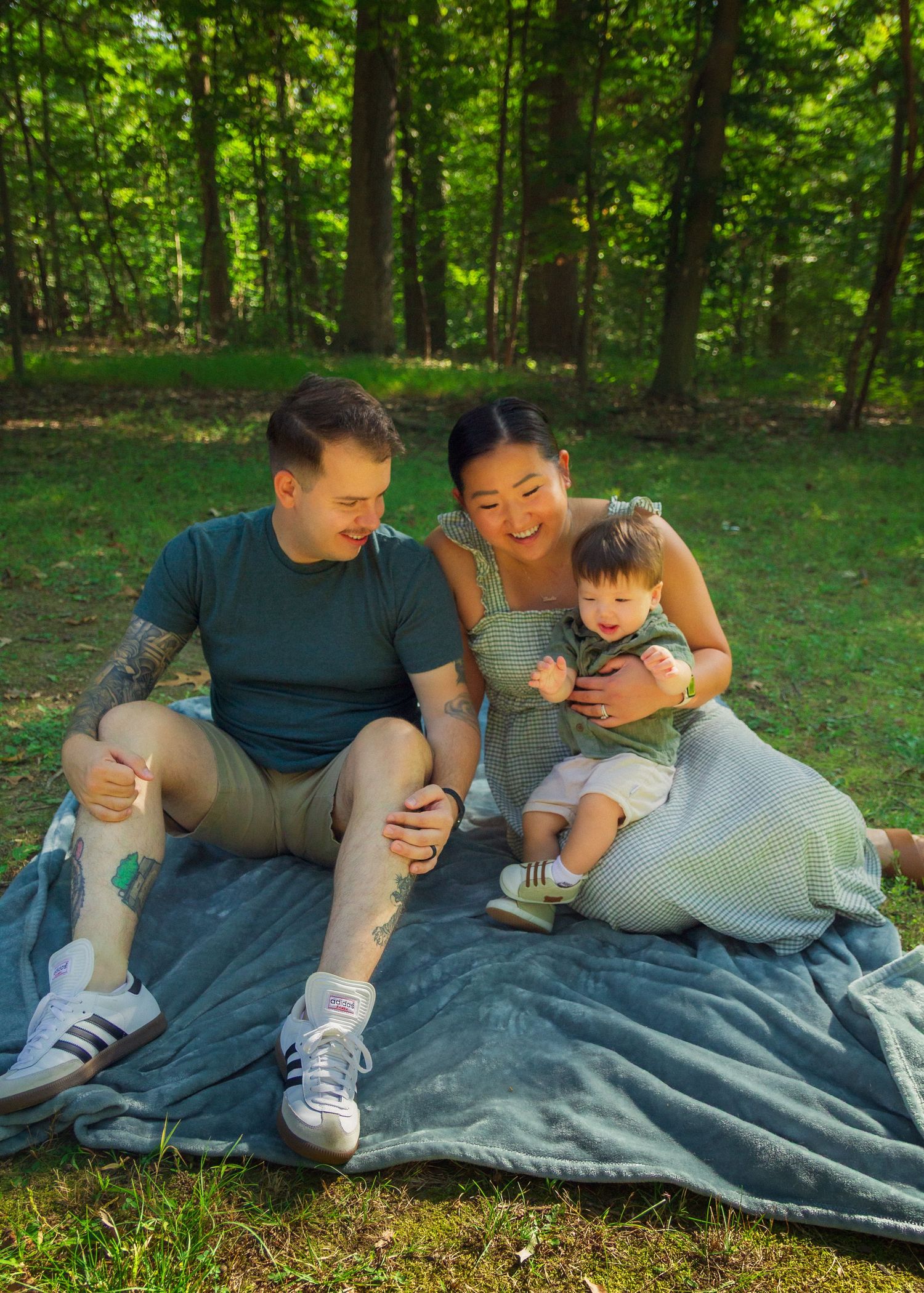 Family members relaxing together on a blanket outdoors in a wooded area during a summer day.