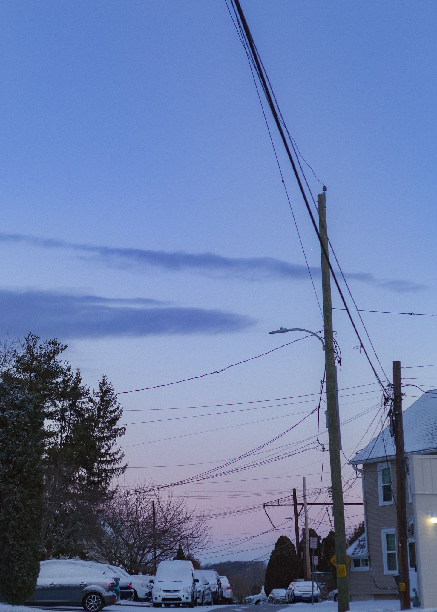 A panoramic view of utility poles and power lines silhouetted against a purple and blue sunset sky.