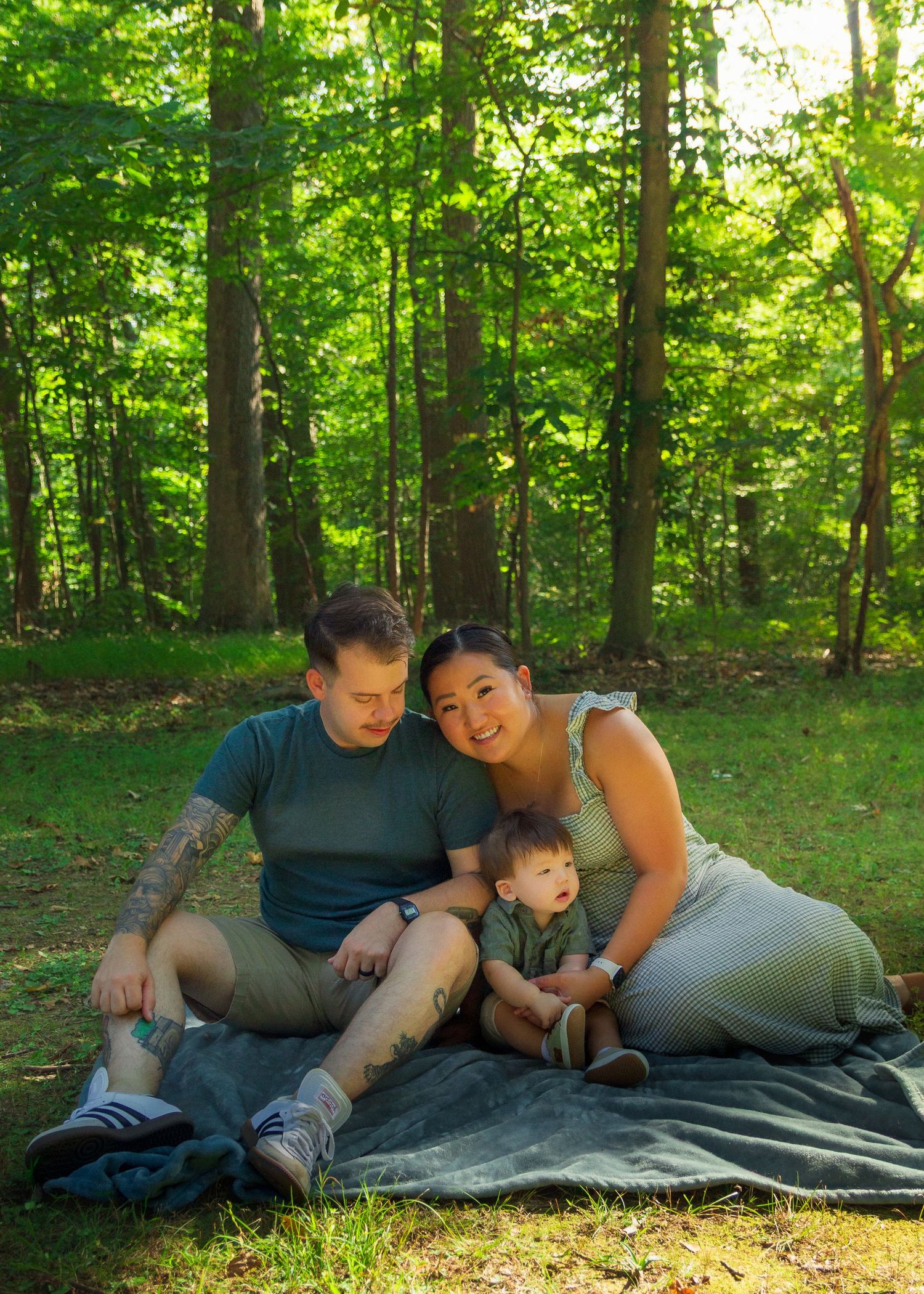 A family relaxes together on a blanket in a sunlit forest clearing during a summer afternoon.