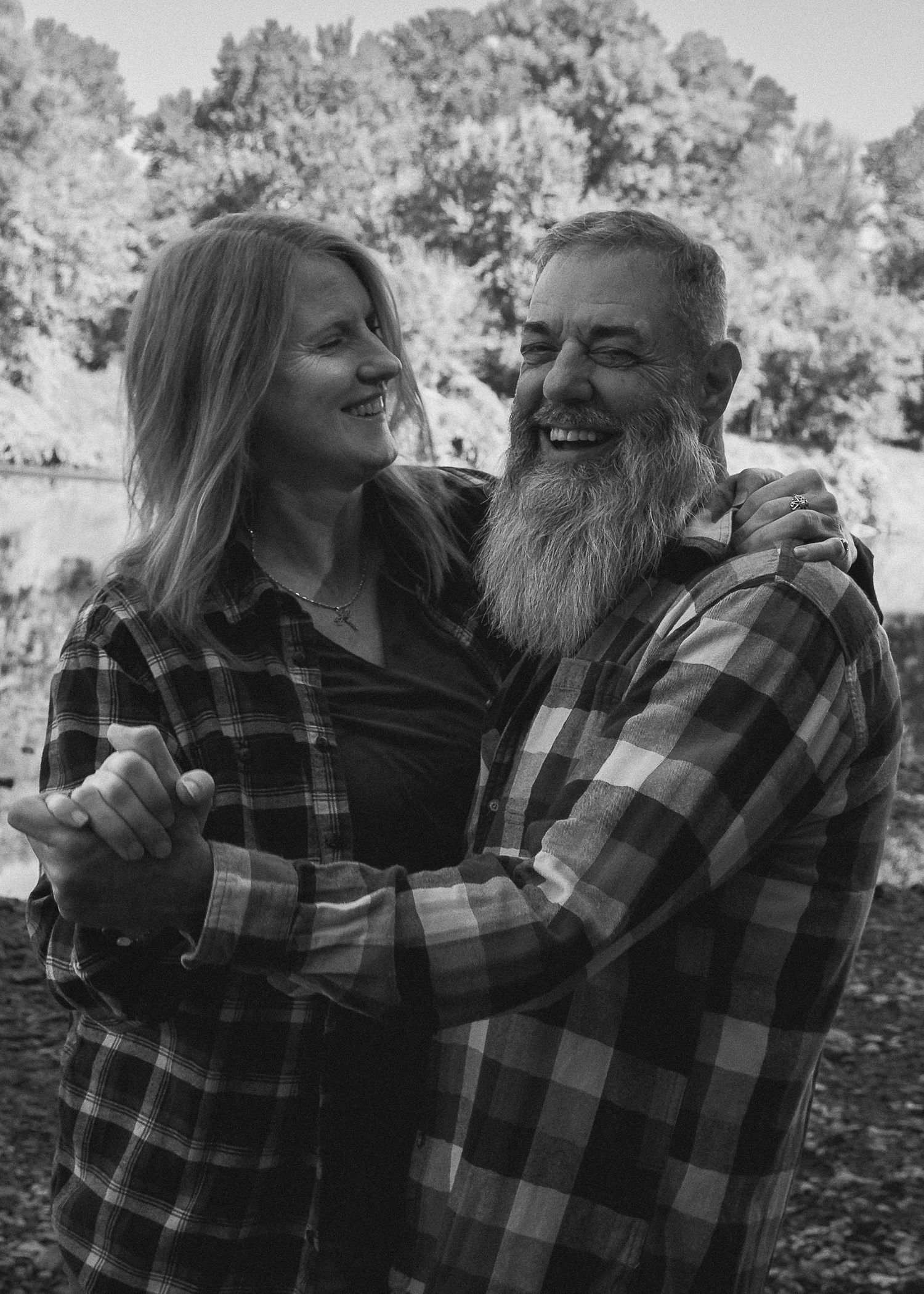 A couple in matching plaid shirts share joyful moments together in a black and white photo series outdoors.