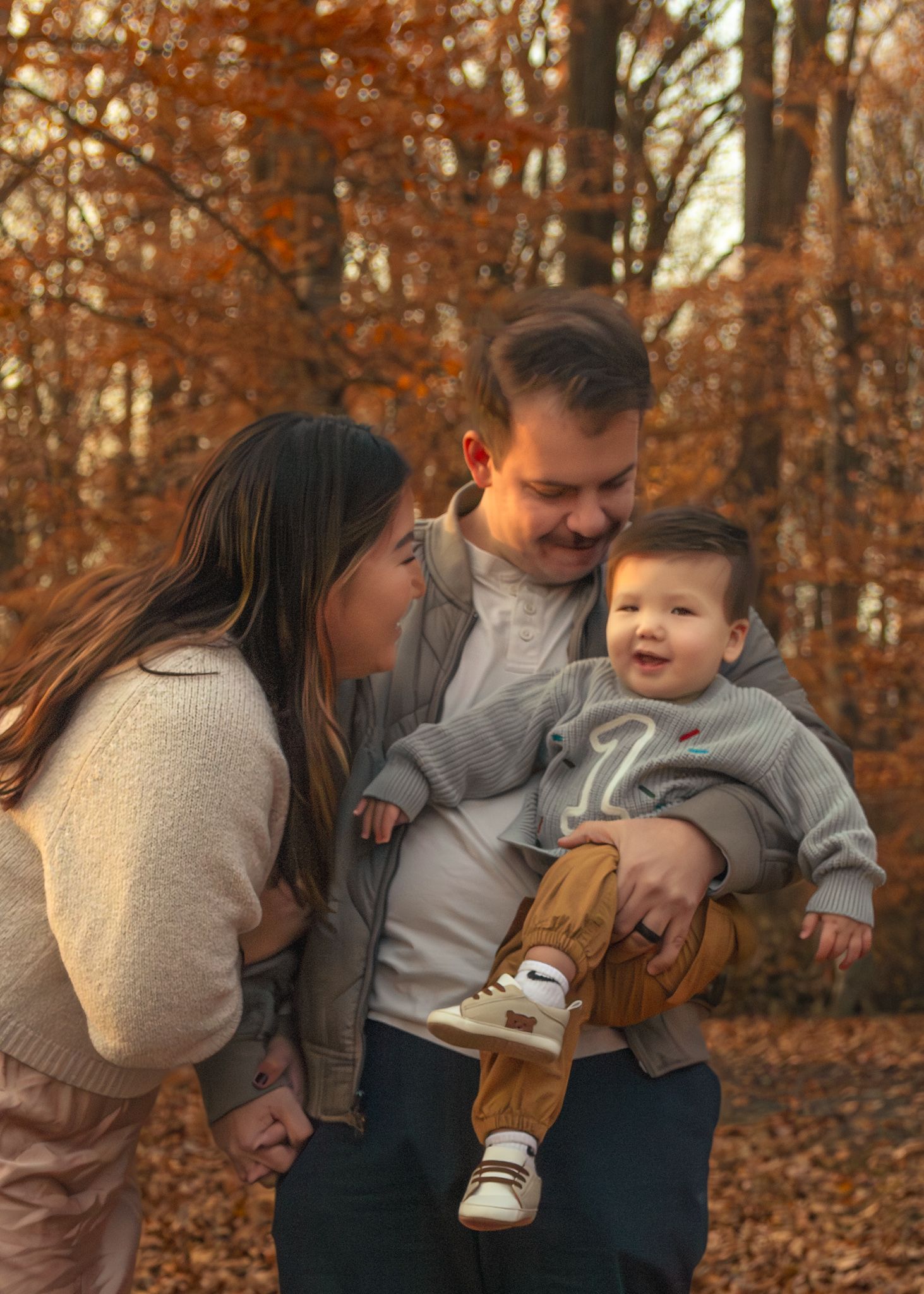 A family shares a joyful moment together on fallen autumn leaves in a forest with orange foliage.