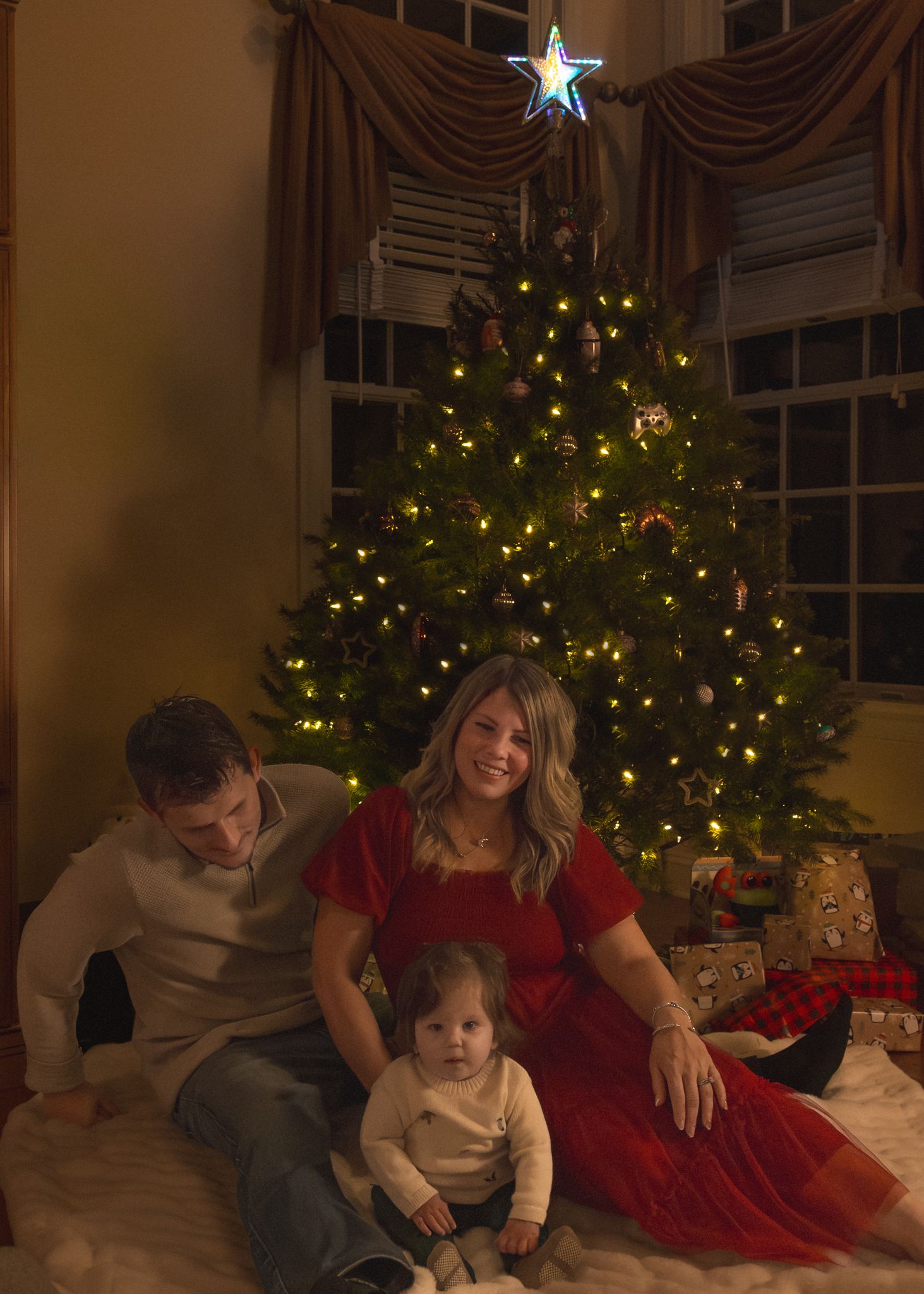 Family sits together near a decorated Christmas tree in a living room with twinkling lights and holiday decor.