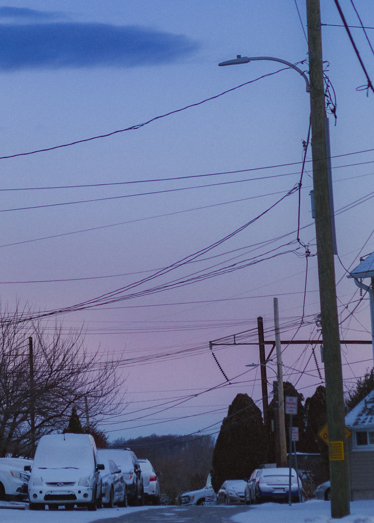 Power lines and utility poles silhouetted against a dusky blue sky in a residential neighborhood.