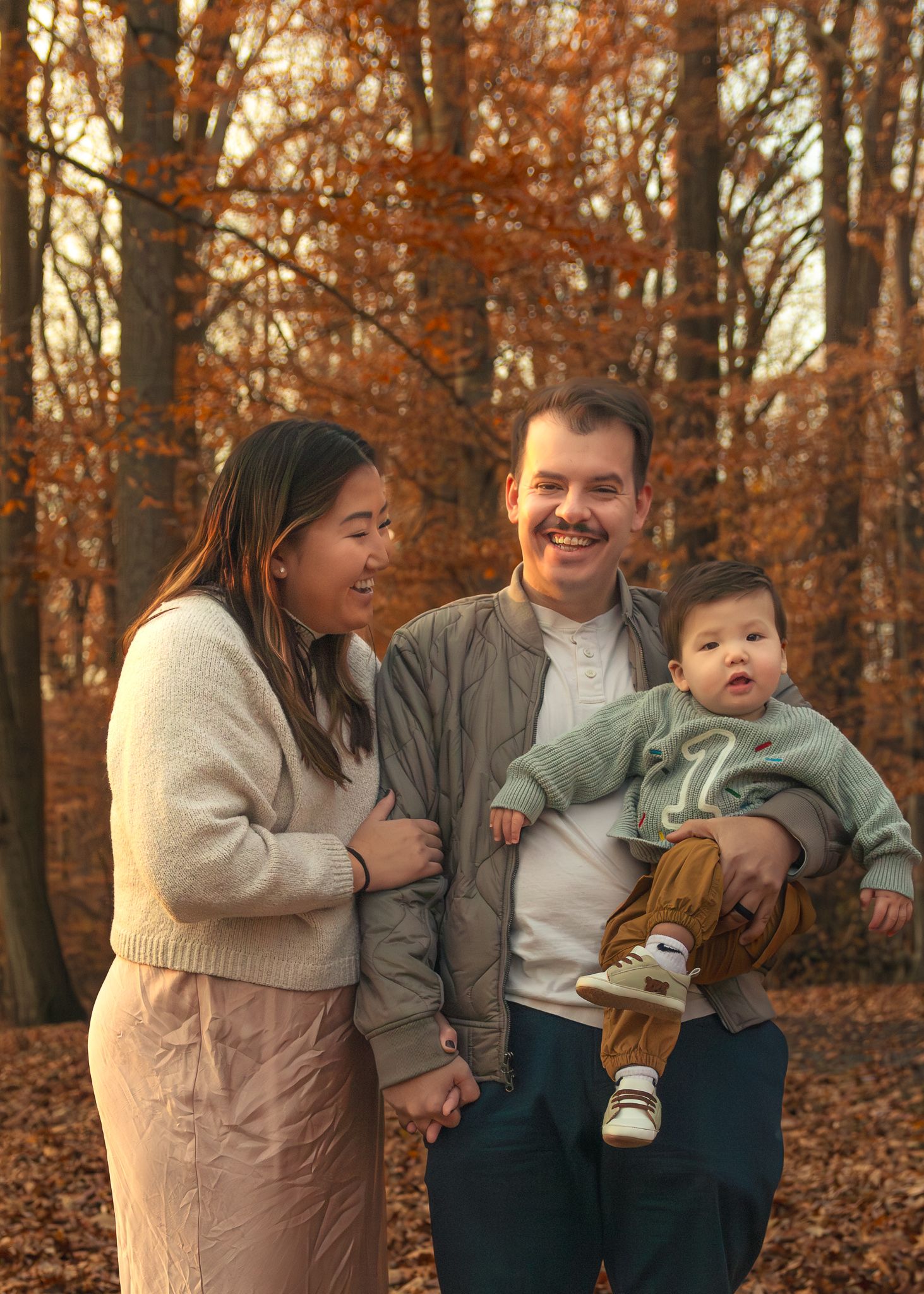A family shares playful moments together on fallen autumn leaves in a forest setting during golden hour. Family Photos Montgomery County PA