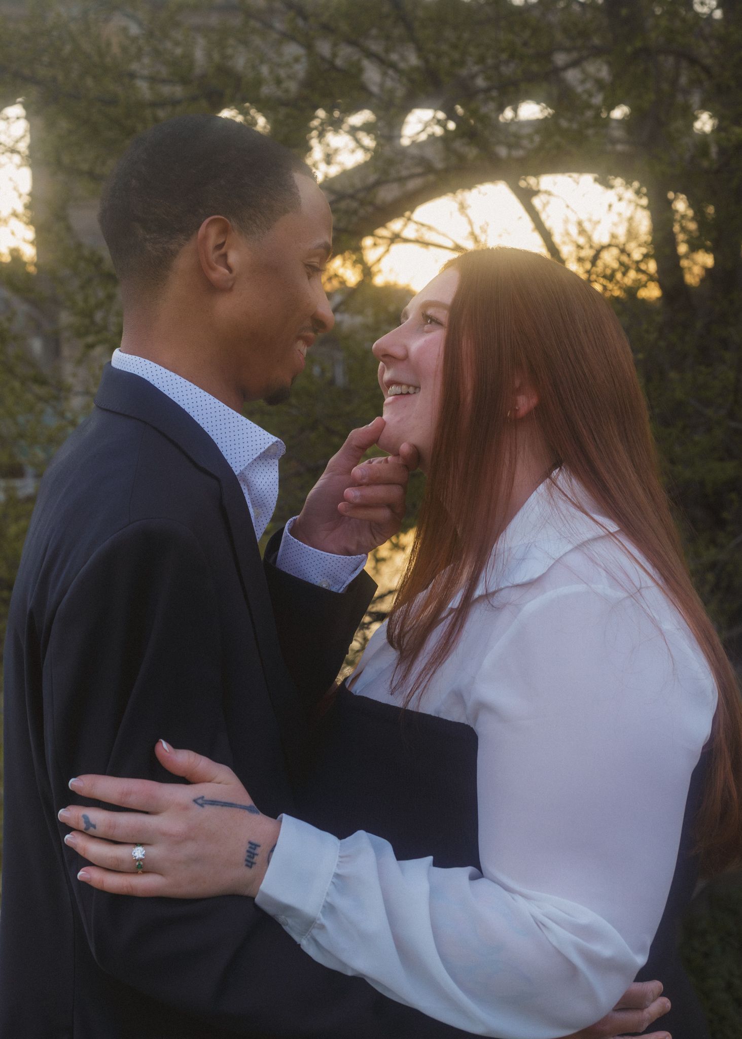 Couple sharing a romantic moment at sunset, man in suit gently touching womans face, woman in white blouse smiling warmly.