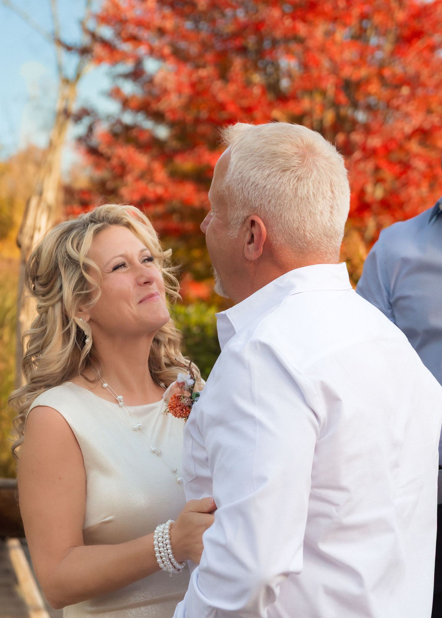 A couple embraces and dances together against a backdrop of vibrant red autumn foliage in a romantic outdoor setting.