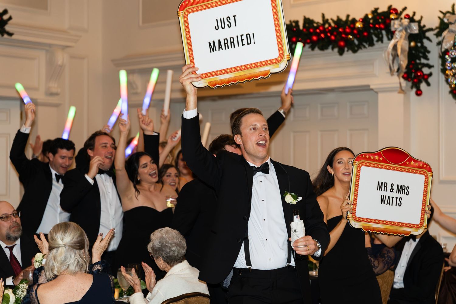 Wedding party celebrates with glow sticks and Just Married signs at festive indoor reception.