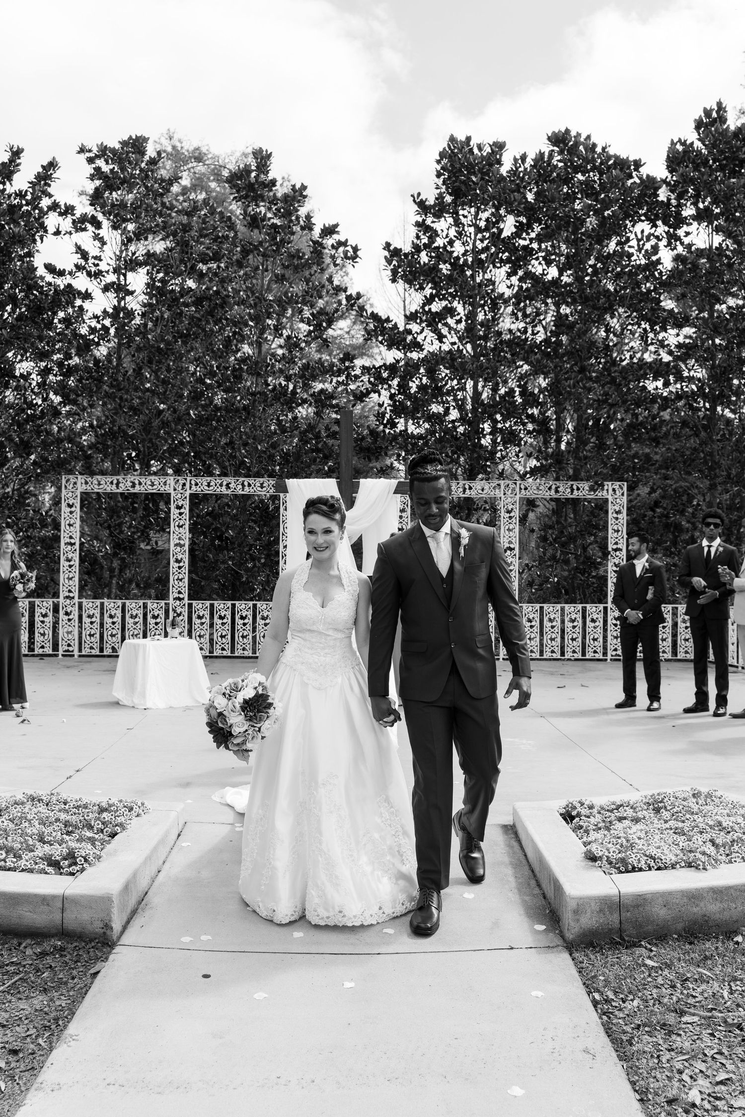 Black and white photo of a newlywed interracial couple walking down the aisle after their outdoor wedding ceremony.