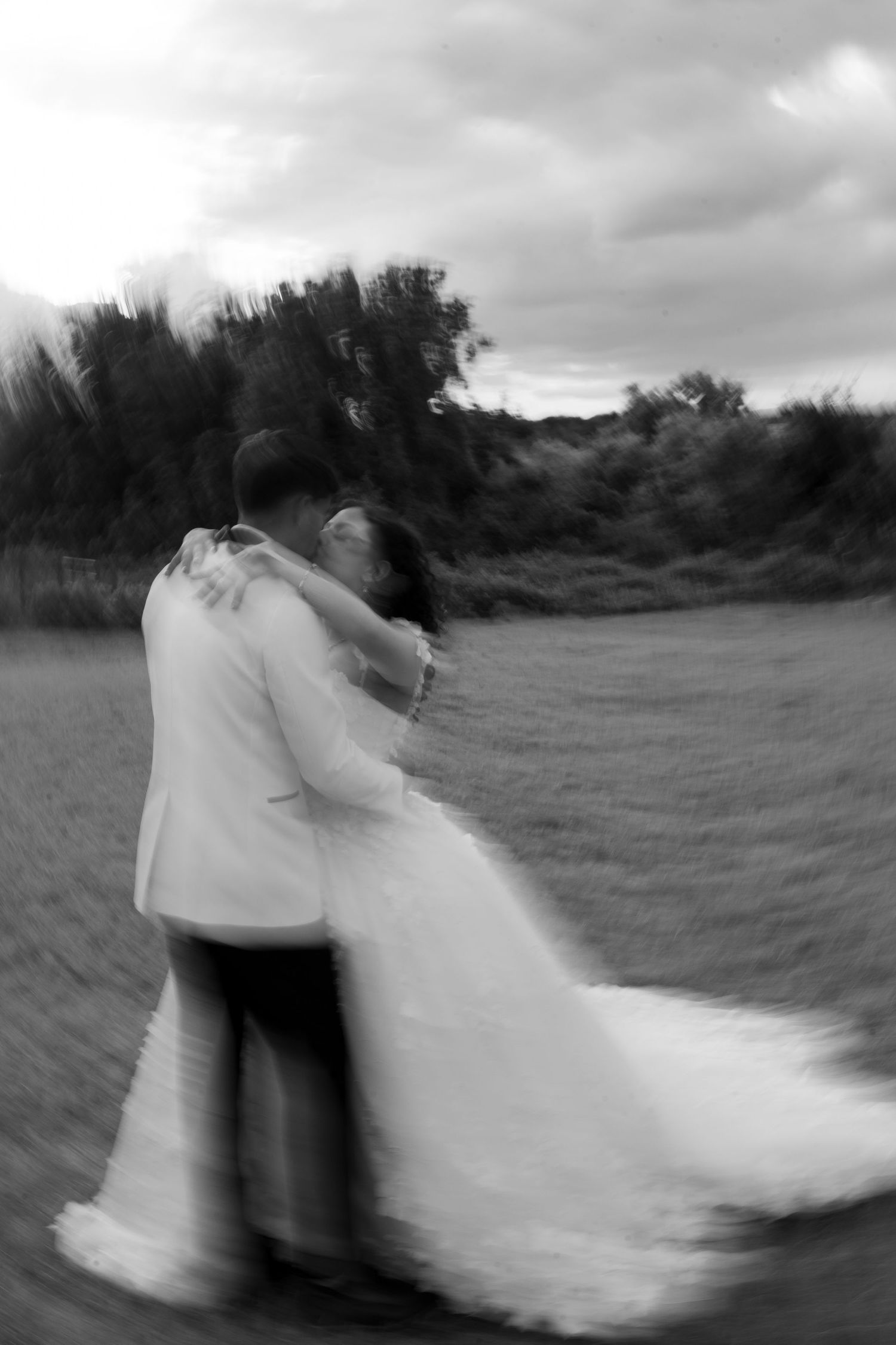 A bride and groom share a romantic embrace in a field in this artistic blurred black and white photo.
