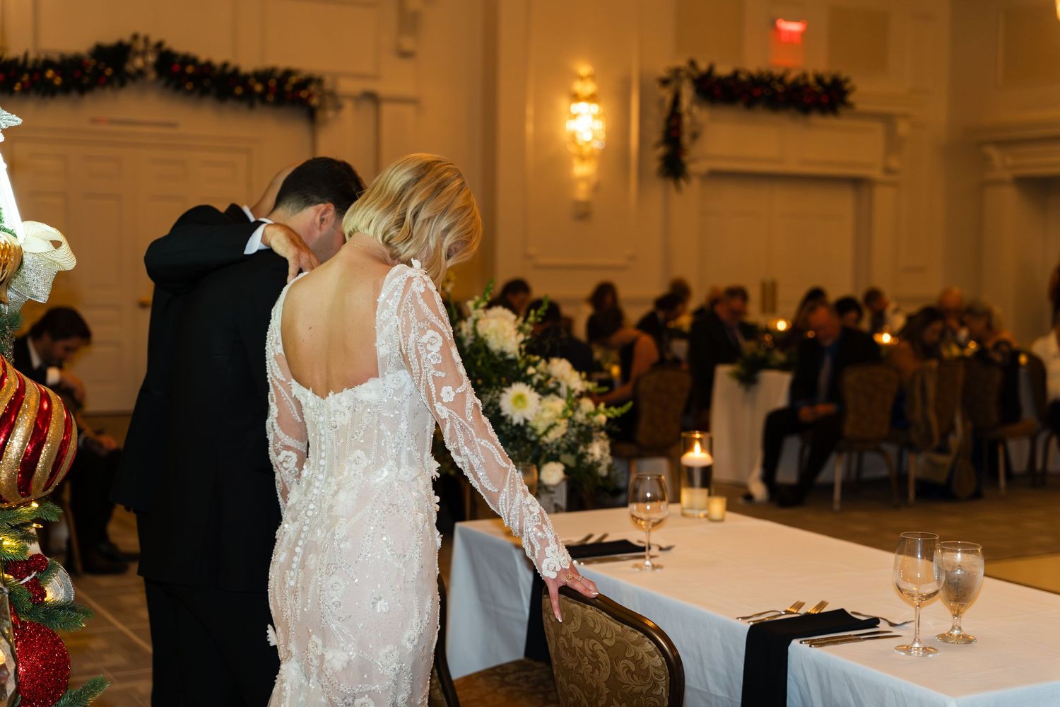 Bride and groom hold hands at sweetheart table during elegant ballroom wedding reception.