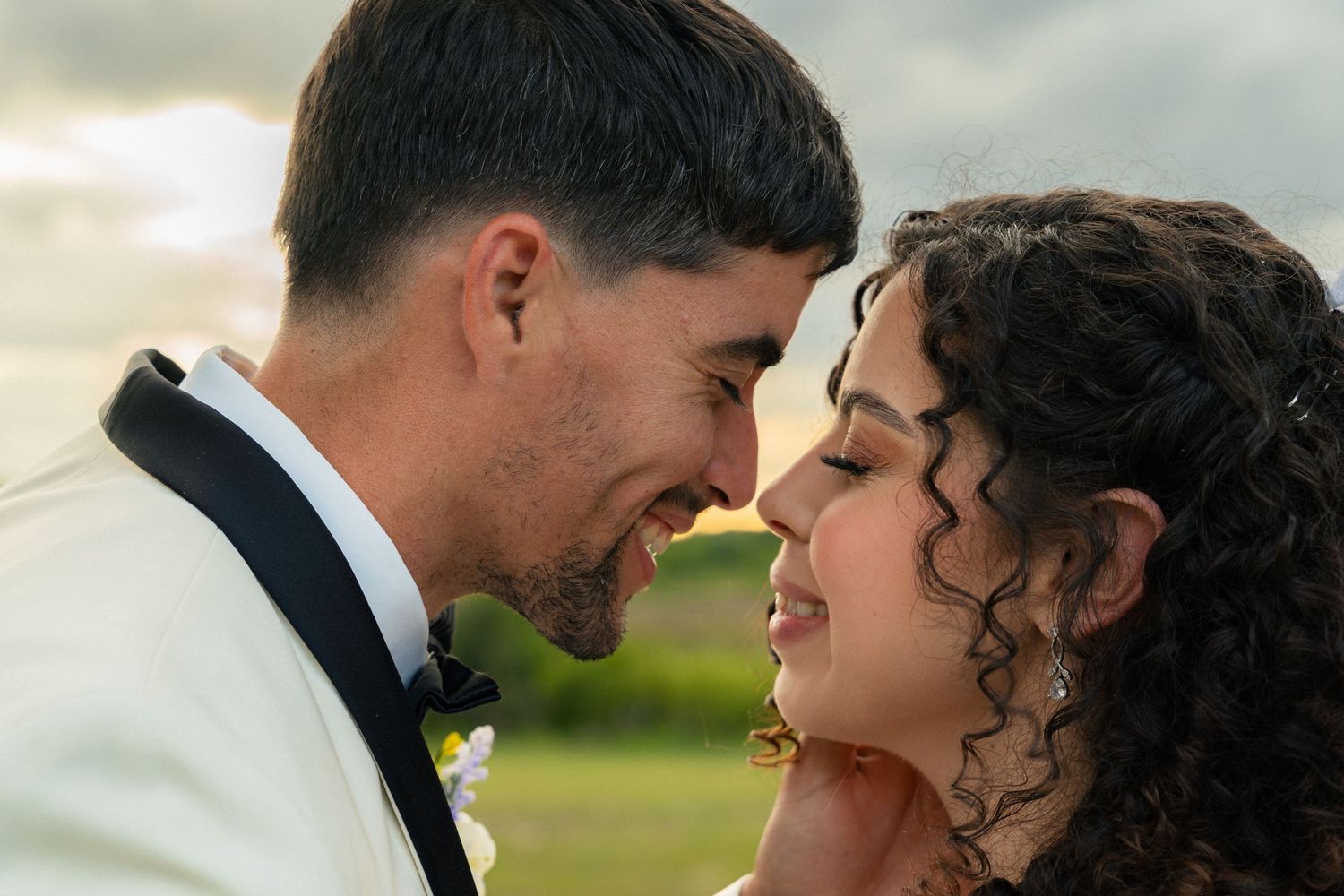 Bride and groom share a tender forehead-to-forehead moment in a romantic close-up portrait at sunset.