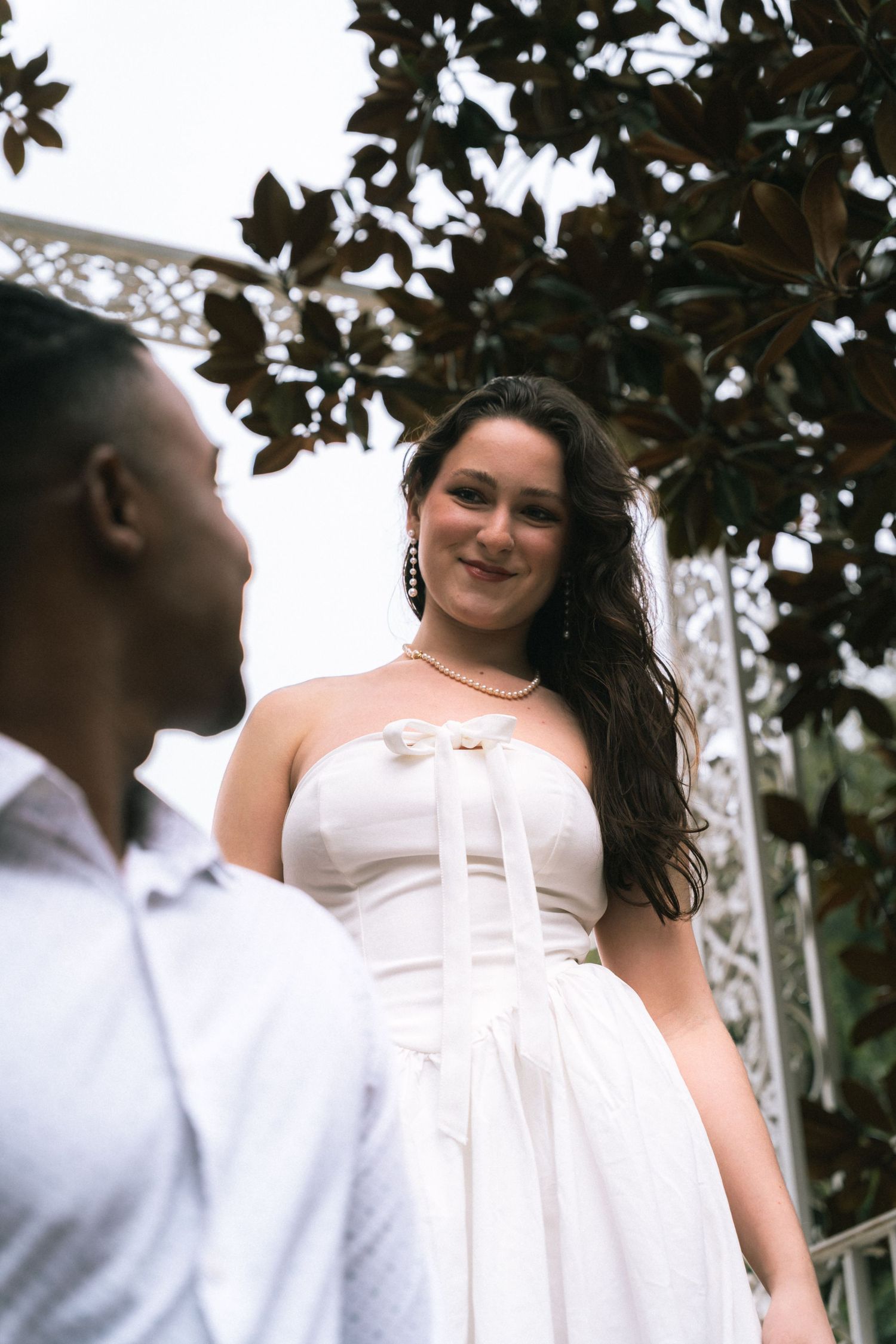 A romantic outdoor portrait of a couple among magnolia leaves, with one wearing a white strapless dress.