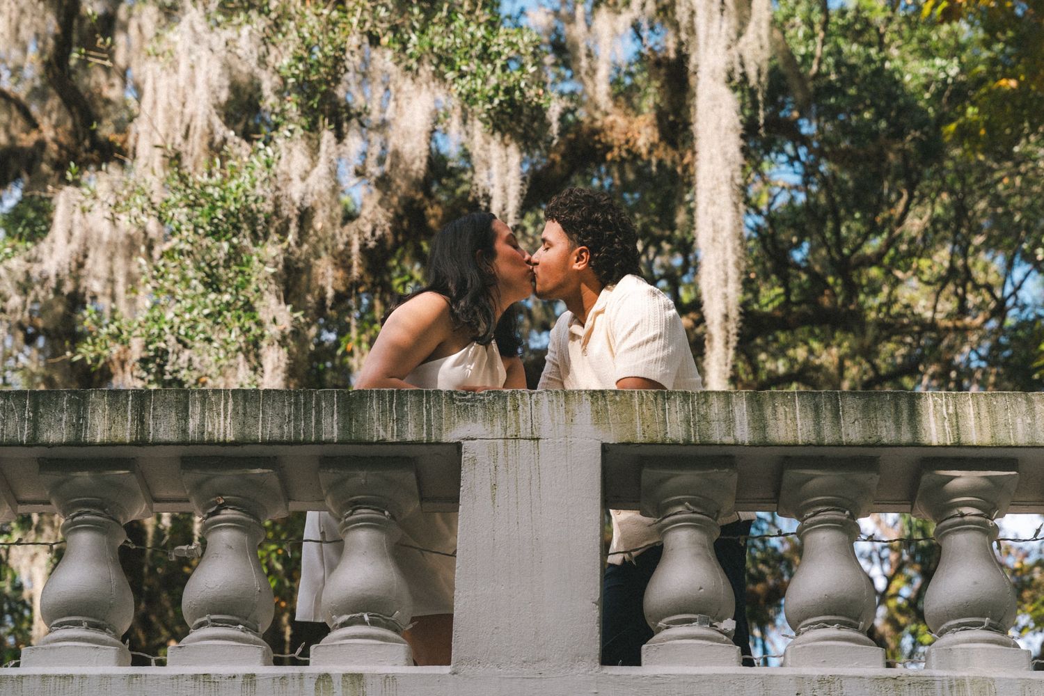 A scenic Spanish moss-draped oak tree lined pathway with white columns and people walking in the distance.