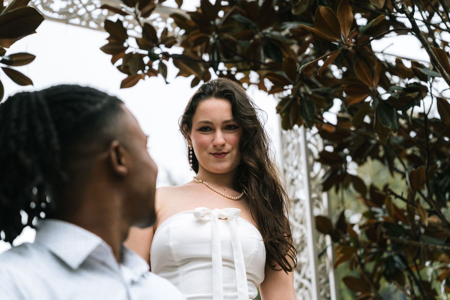 A couple shares intimate moments during an outdoor photoshoot among trees with brown leaves.
